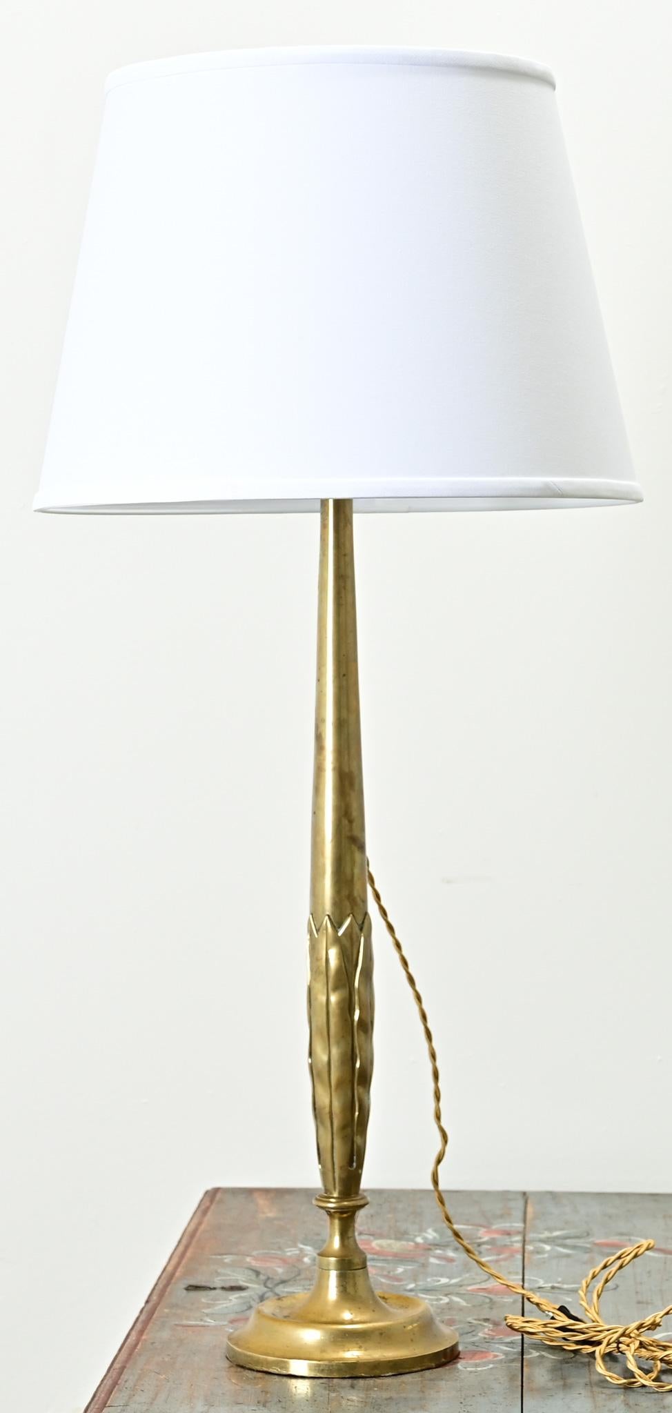 A tall and slender solid brass table lamp from France. A statement lamp, simple in design, with foliate details is lifted on a brass pedestal. This fixture has been recently wired for US electrical using UL listed parts with a new linen drum shade.