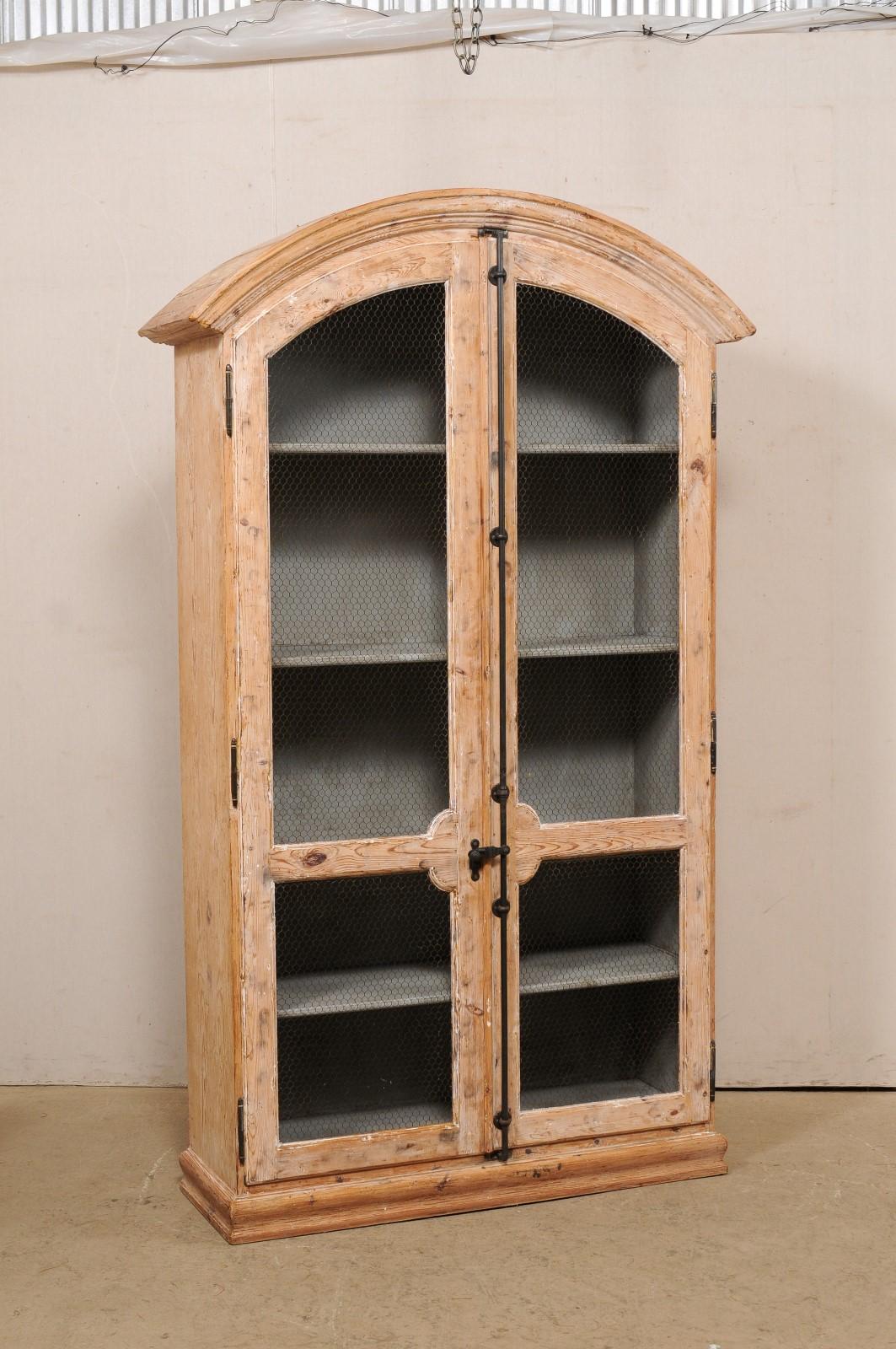 A vintage French two-door bleached wood tall display cabinet. This tall French cabinet features an elegantly arched crest top, over a pair of doors, whose tops are cut to mimic the arched top, and is raised on a flat base. The doors are each fitted