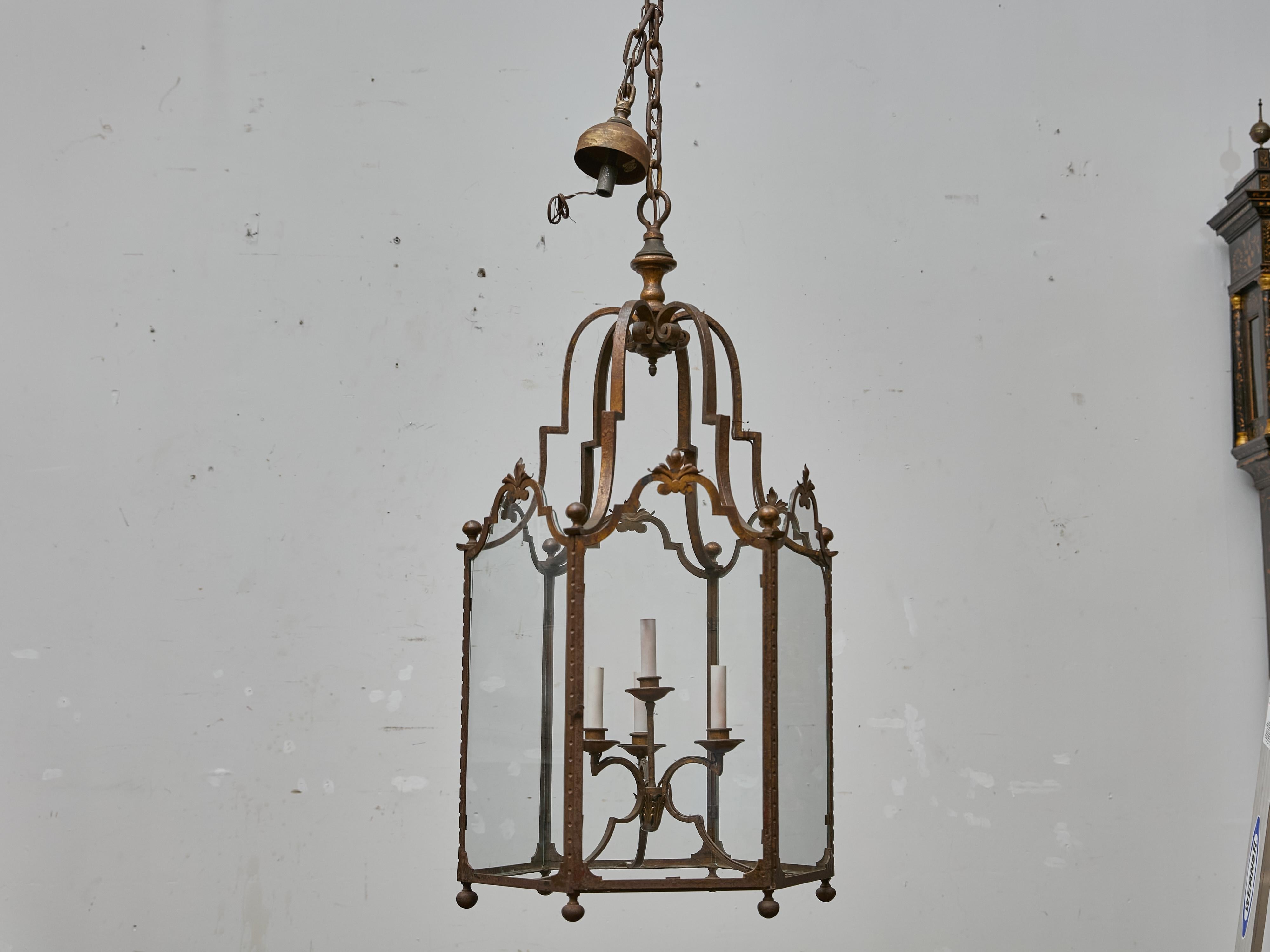 Esta gran linterna francesa de hierro de hacia 1900 presenta una elegante forma arquitectónica hecha de hierro remachado con acabado original patinado y paneles de cristal transparente en todos los lados. La silueta calada presenta arcos festoneados