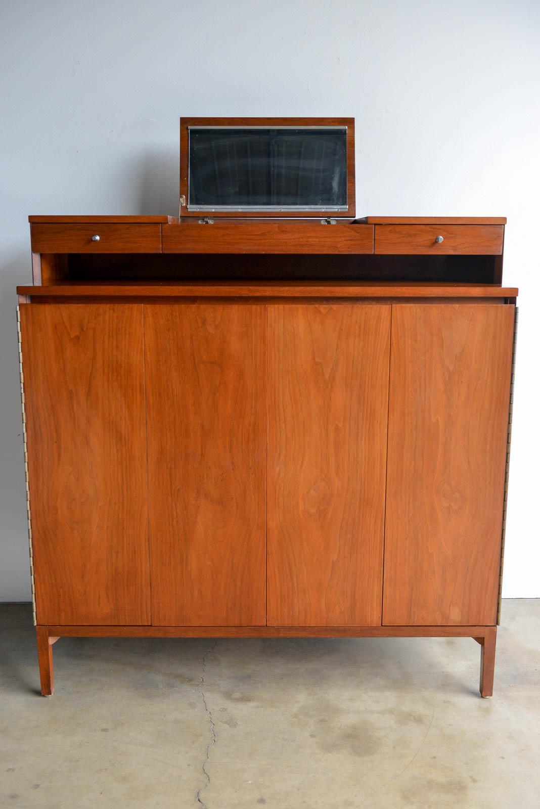 Tall gentlemen's chest in walnut by Paul McCobb, circa 1960. Flip up mirror with original plug-in A/C outlet. Walnut finish in good original condition with slight wear, as expected. No major dings or scratches. All drawers are leather lined and left