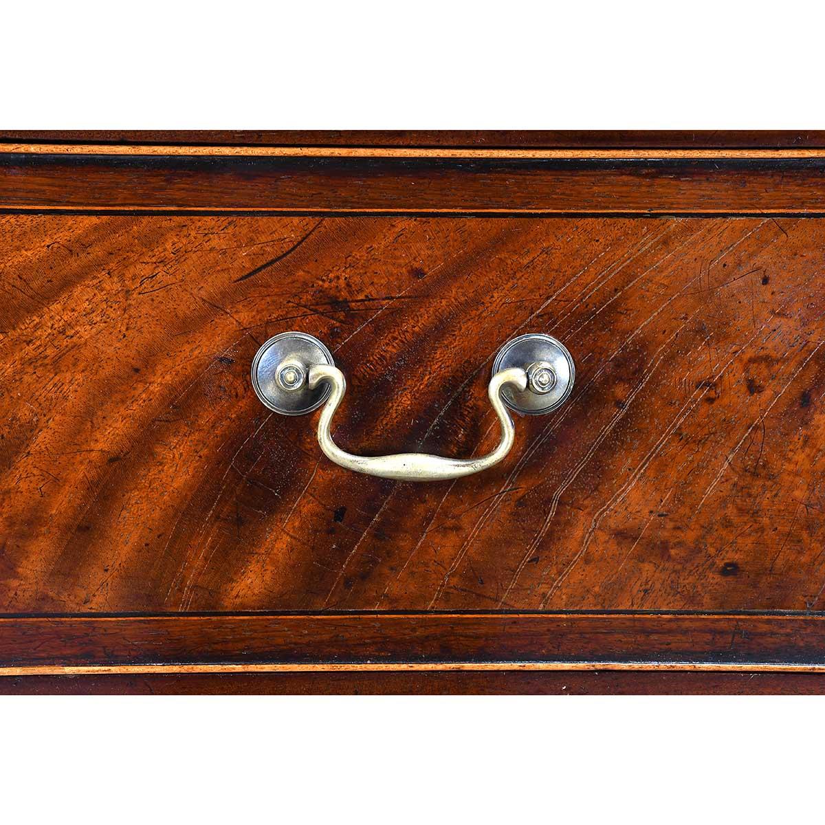 Alta cassettiera in mogano di epoca Giorgio III con sette cassetti graduati. Ciascun cassetto è bordato a croce e intarsiato con stringhe a contrasto. Eccezionale mogano figurato sui frontali dei cassetti e patina eccezionale. Si regge su piedi a