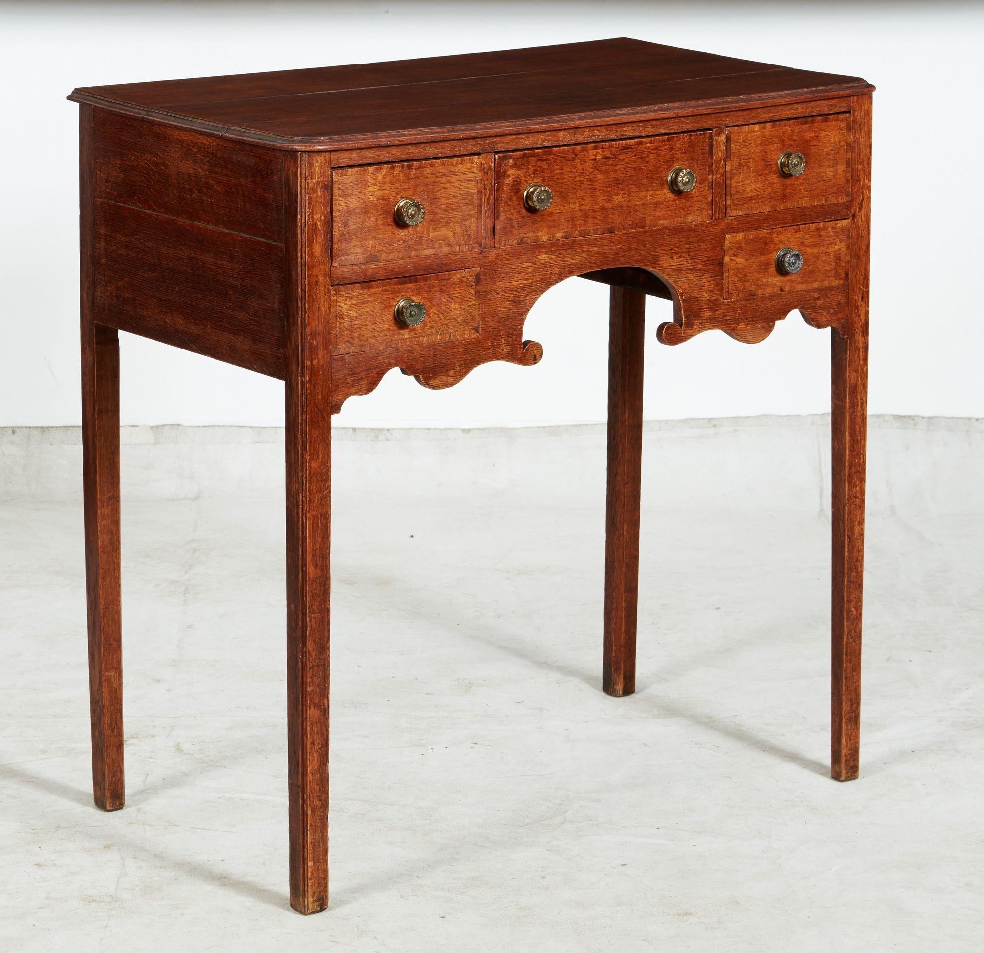 An elegant lowboy or side table in quarter sawn oak having three plank top with molded edge and rounded corners over three drawers with longer center drawer over two lower drawers all with cross-banded edges, and featuring a boldly shaped apron with