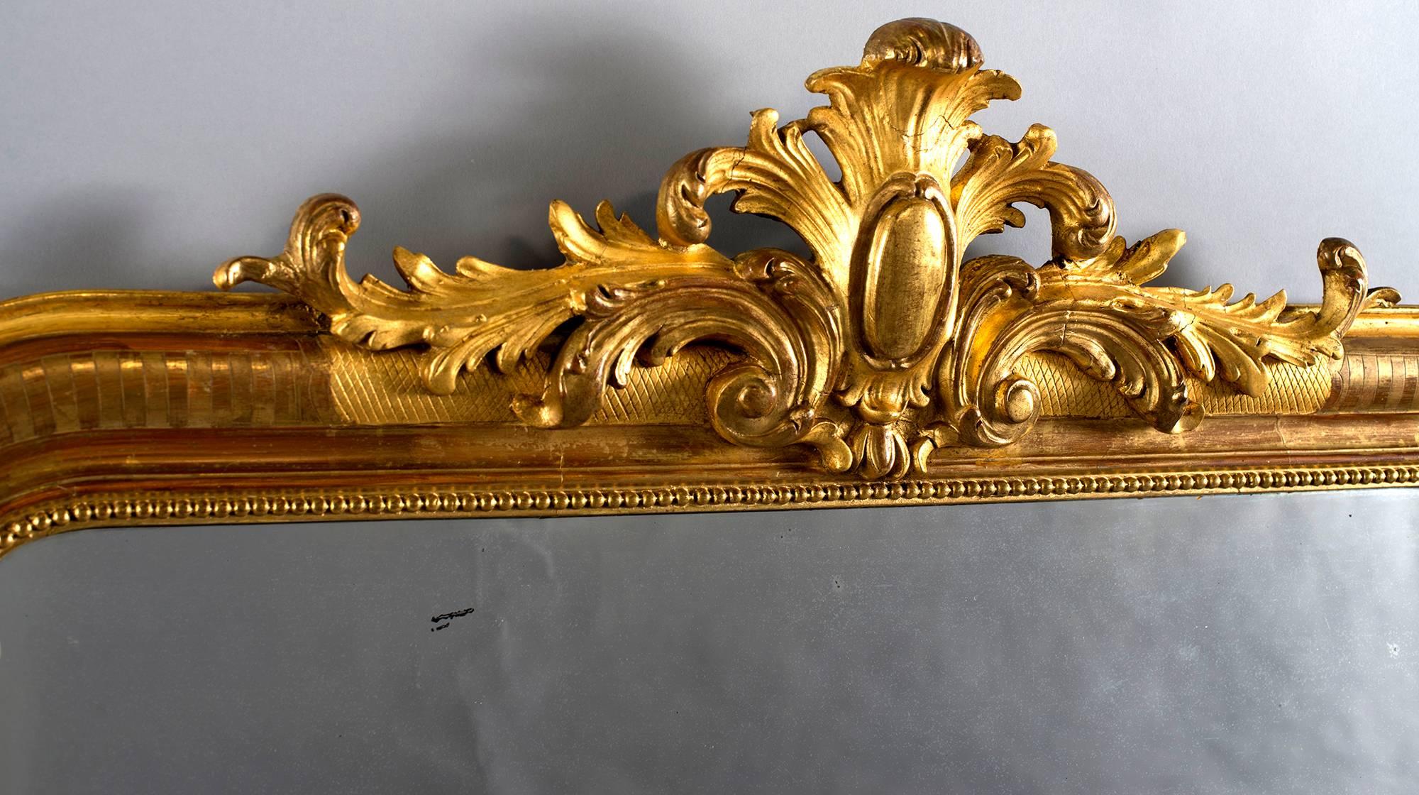 French Louis Philippe style mirror has gilded wood frame, inner beaded edge and elaborate carved and sculpted ornamental crest, circa 1860s.  Actual Mirror Size:  50” h x 31” w