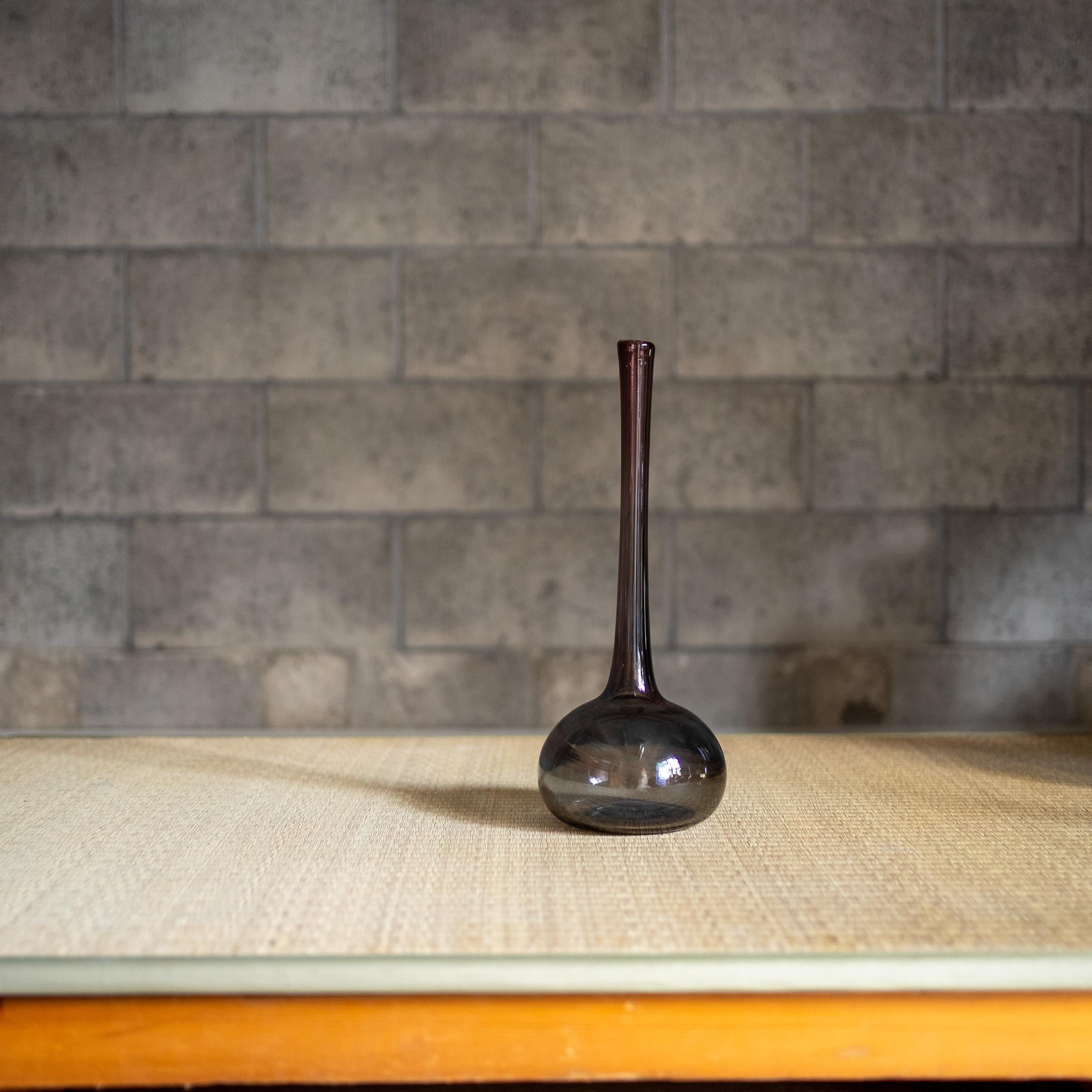 A striking hand-blown glass vase by French artist Claude Morin. Its elongated neck rises gracefully from a rounded base, giving the piece a sculptural silhouette with a strong vertical rhythm.

The dark purple, subtly tinted glass carries both depth