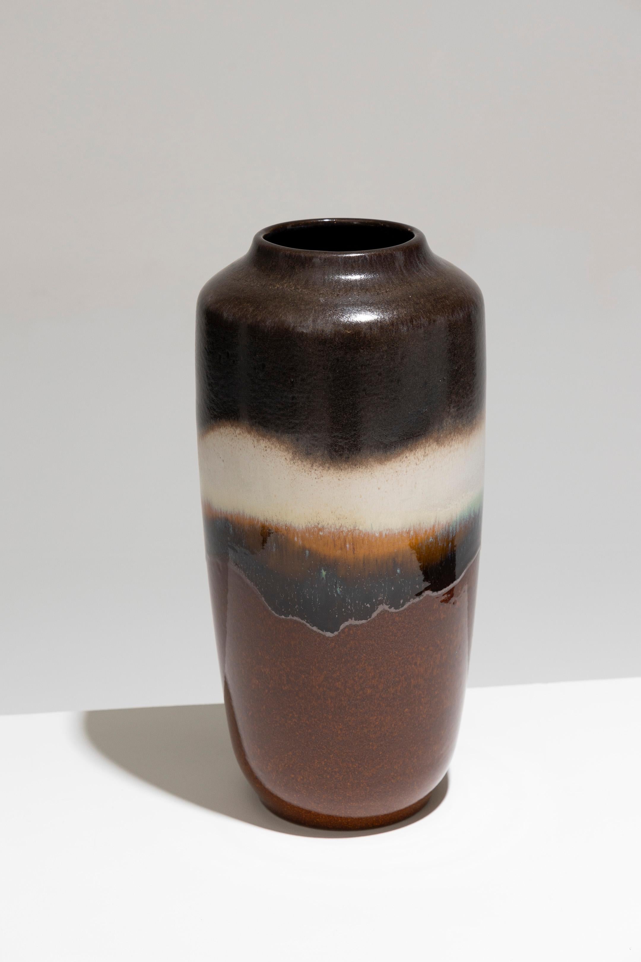 Tall Glazed Pottery Vase, West Germany, 1960s. The vase features a tall body with a slight shoulder and a round mouth. Its decoration consists of horizontal bands in varying colors and textures. The largest band at the base is a glossy rust-brown