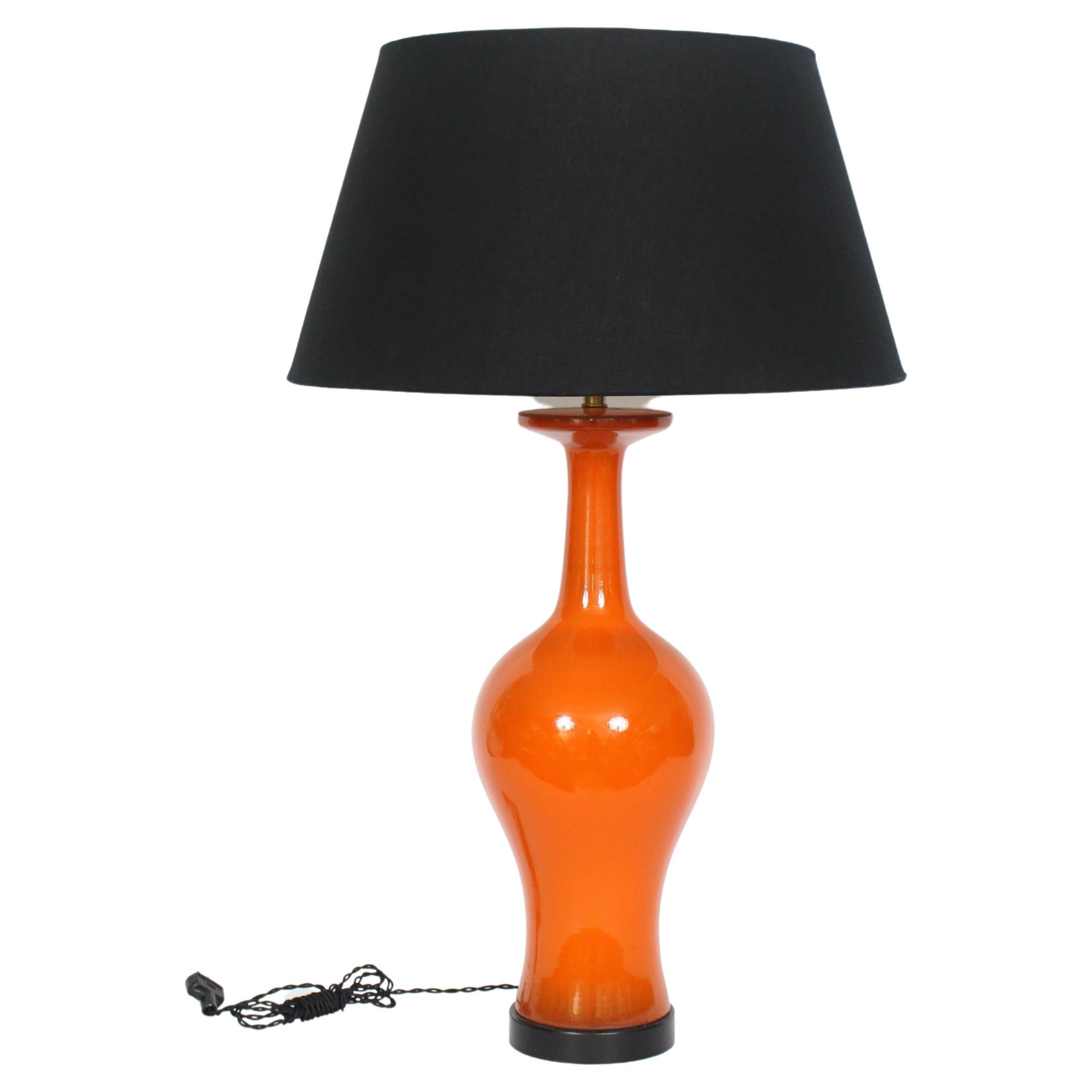Statuesque Modernist Glazed Red Orange Ginger Jar Pottery Table Lamp. Featuring a clean reflective surface a top a circular Black enameled metal base. Small footprint. 28H to top of socket. 21H to top of Ceramic. Classic. Timeless. Fine design.
 