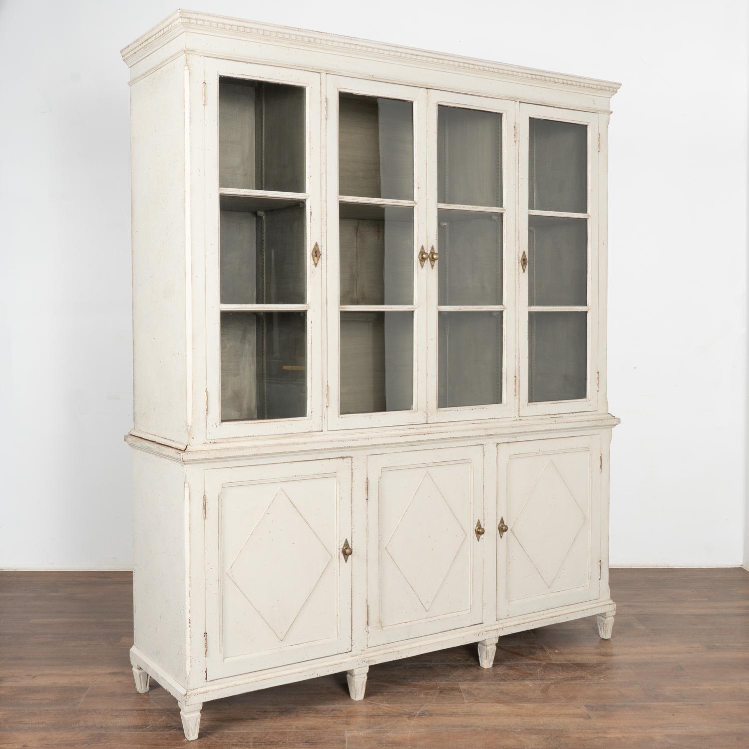 Elegant and stately Swedish Gustavian style display cabinet or bookcase in two sections standing just under 7' tall.
Newer professional painted finish in softly distressed light grey fitting the age and grace of this timeless piece.
Adjustable