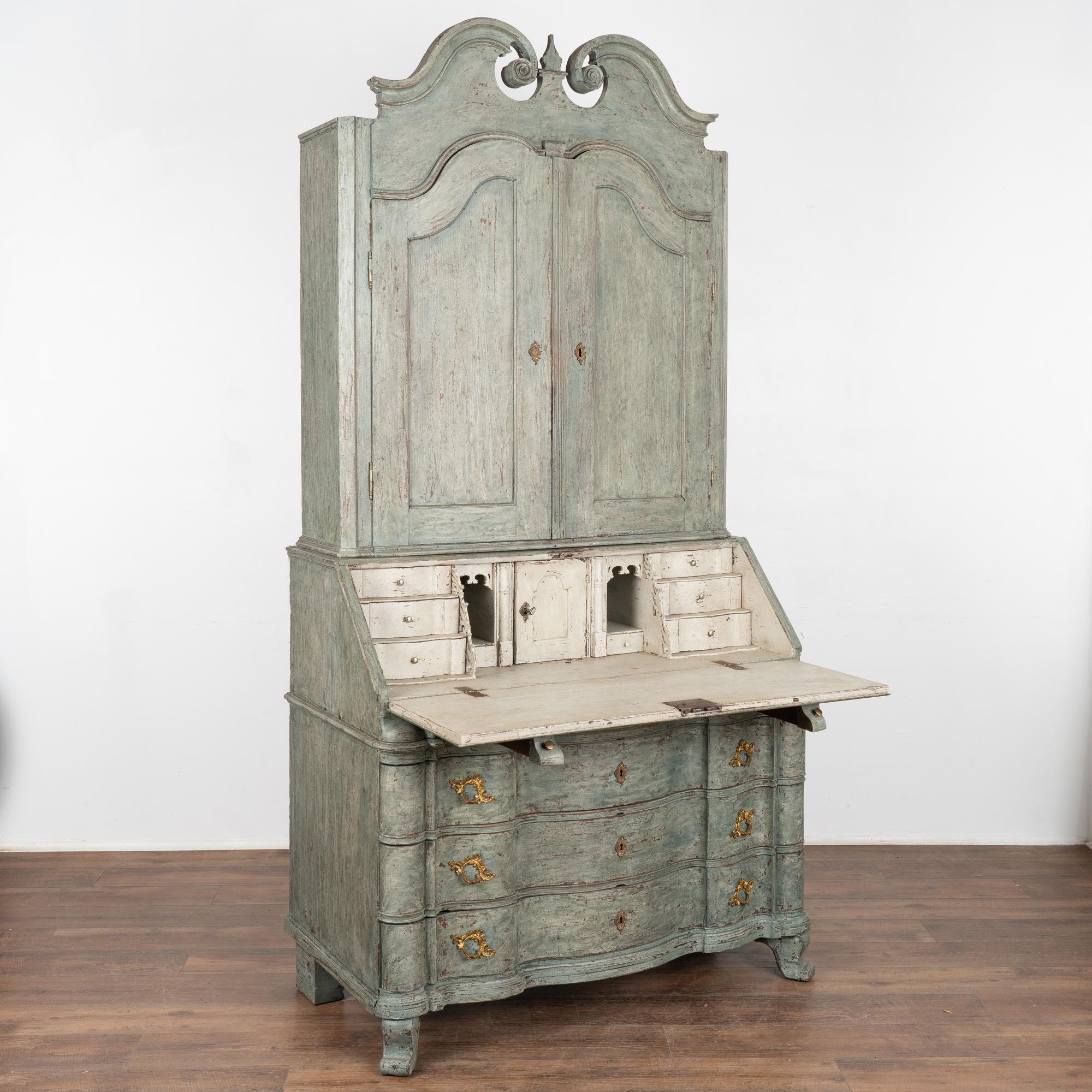 This striking oak secretary is an elegant statement piece crowned with an elaborate carved pediment.
The secretary has been given a professional custom teal green layered/striated painted finish which has been gently distressed to reveal the