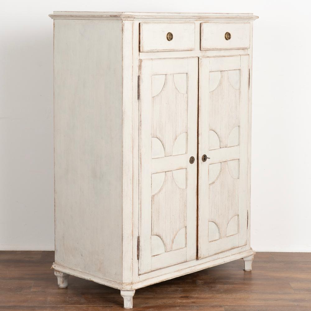 Gustavian tall pine cabinet or sideboard; two drawers over two doors. 
Decorative fluted panels and tapered feet.
Newer, professionally applied layered white painted finish (with light gray undertones) slightly distressed to fit the age and grace