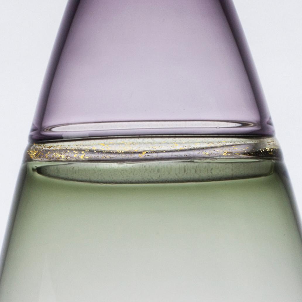Tall and voluminous, this hand blown art glass statement vase features sage green and indigo violet translucent hues. A gold-flecked seam fuses the colors at the shoulder. The Goccia (Italian: 
