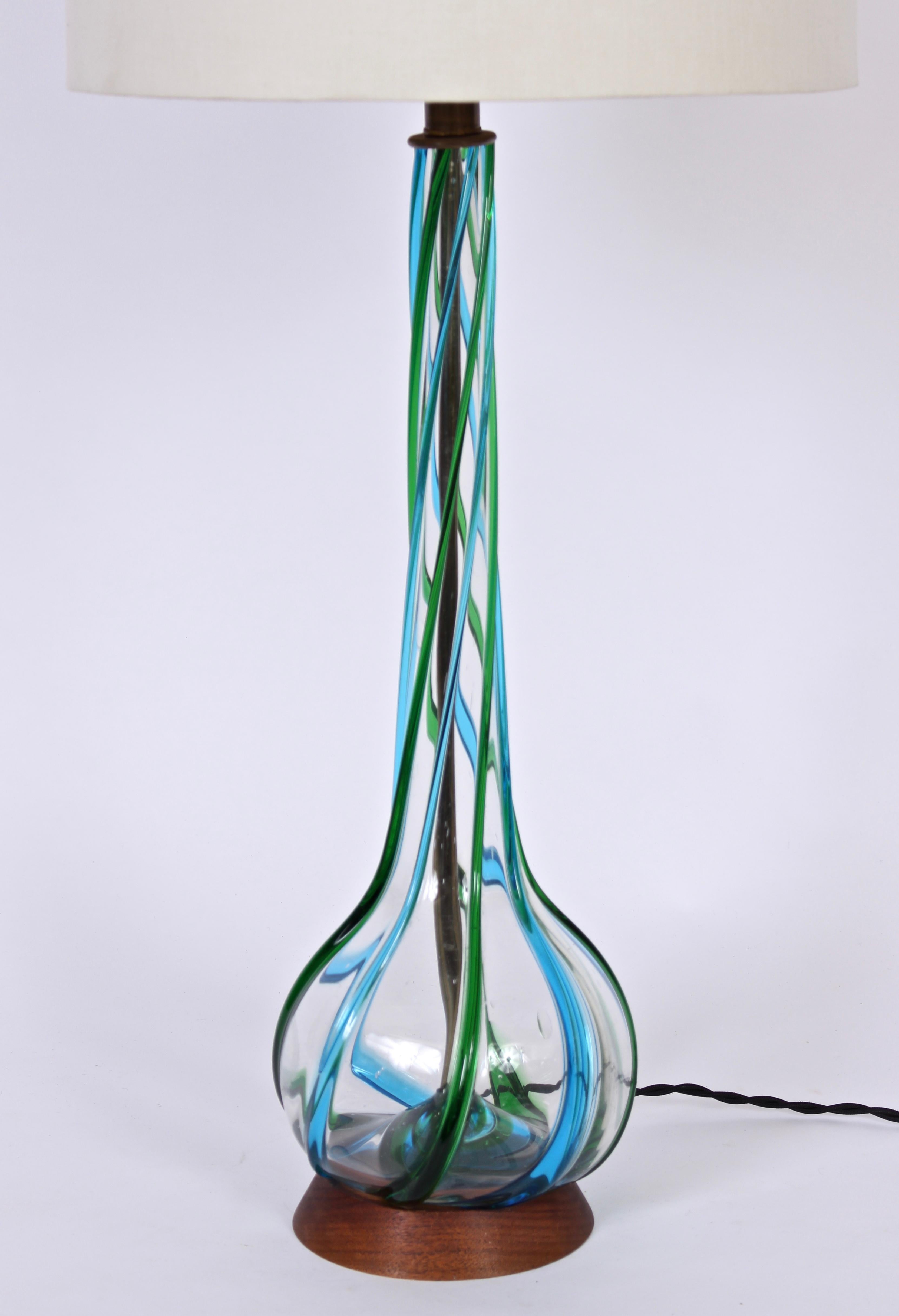 Substantial transparent Murano glass table lamp with applied ribbon relief in peacock blue and green. 35 H to top of finial with harps in place. 26 H to top of socket. Glass 21 H. Shades shown for display only (13 H x 13 D x 14 D). Sculptural.