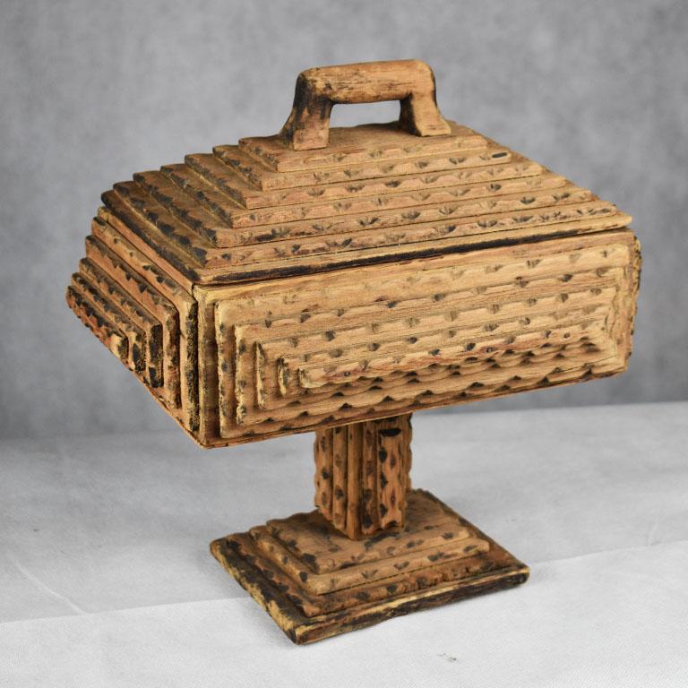 Often known as “prison art” the most widely acknowledged term for this lovely carved wood piece of Folk Art is know as “Tramp Art”. This particular piece is tall and rectangular in shape and sits upon a pedestal base. The top has a removable lid