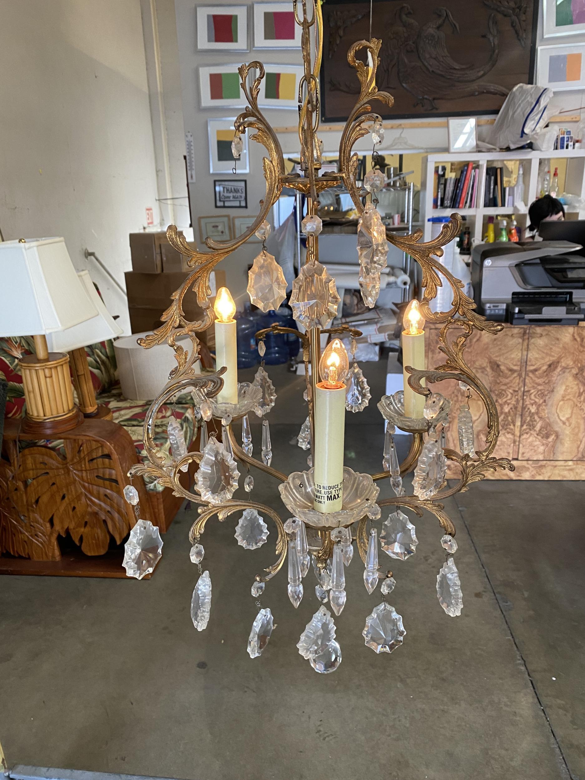Un elegante lampadario Hollywood Regency del XX secolo in cristallo e ottone. Questo lampadario ha tre luci che sono state elettrificate e circondate da cristalli scintillanti.

Misure: larghezza 24