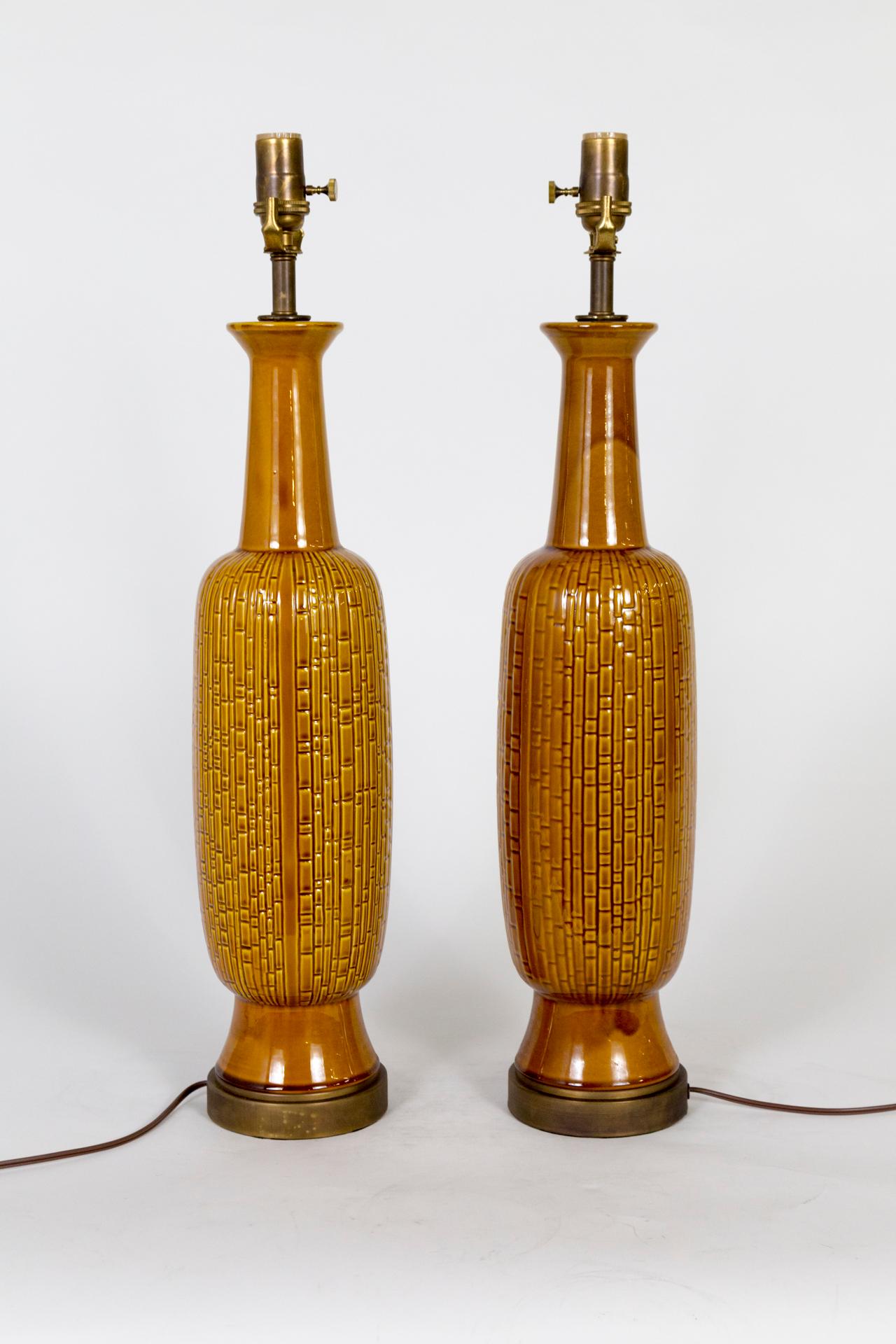 A pair of large, poised, Mid-Century Modern, ceramic lamps with imprinted grooves creating subtle texture; in a versatile, rich honey color, new brass bases, and 3-way socket. Measures: 27