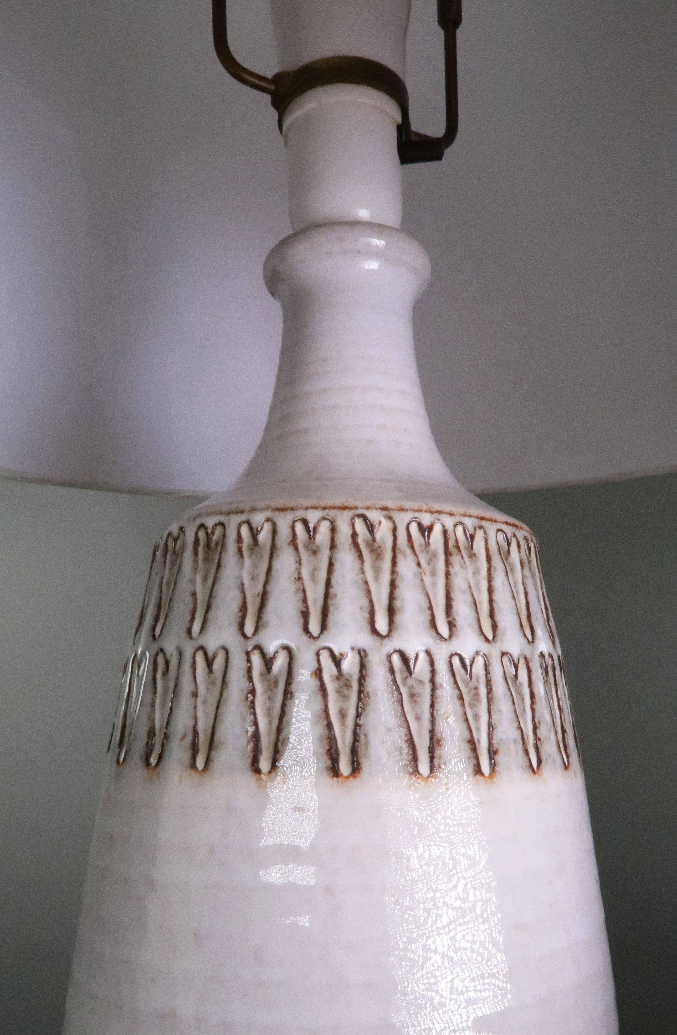 Handmade and hand decorated tall, beautiful and timeless Danish Mid-Century Modern stoneware table lamp from the early 1960s. Manufactured on the Danish island of Bornholm. Warm white, light grey glaze with heart shaped geometric pattern around top