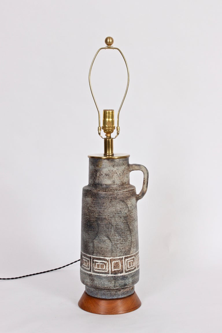 Hand crafted mottled earthen ceramic studio table lamp. Featuring a hand crafted handled pitcher form, layered gray range, vertical texture and bright white detailed Greek key design. On round Walnut base. Shade shown for display only (10 H x 17 D
