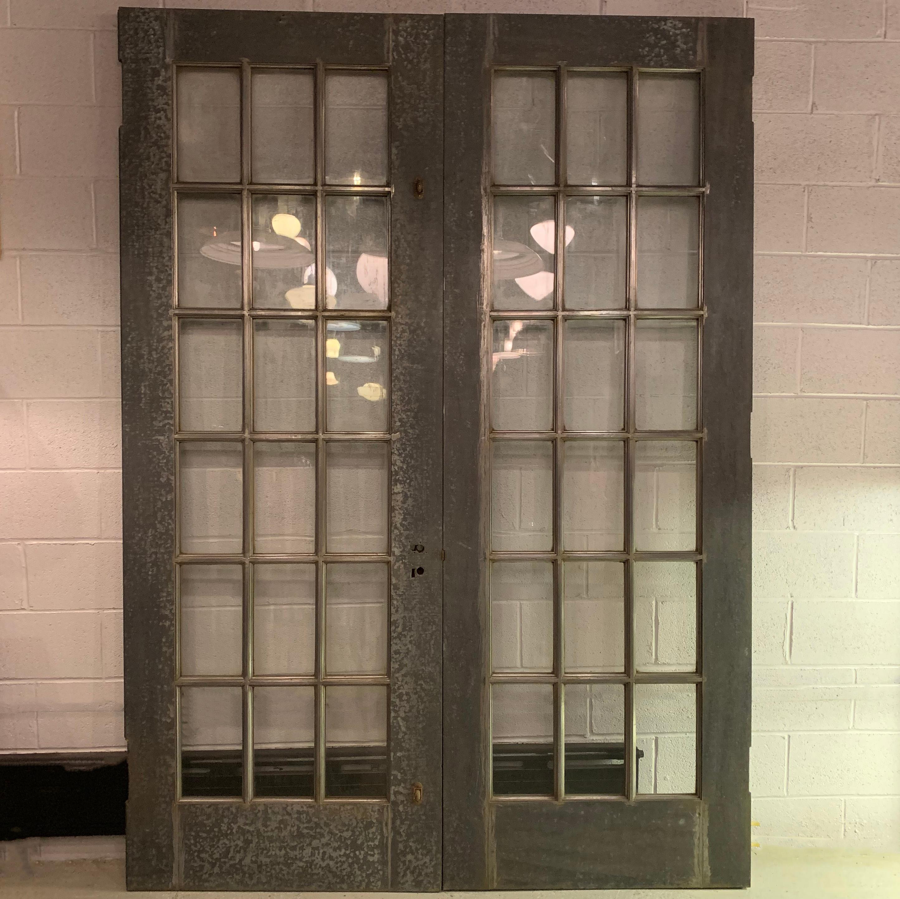 Pair of impressive, Industrial, 8 foot tall, architectural doors feature galvanized steel paned frames with wood cores, glass windows and brass handles. Each door is 34 inches wide. Mounting hardware not included.