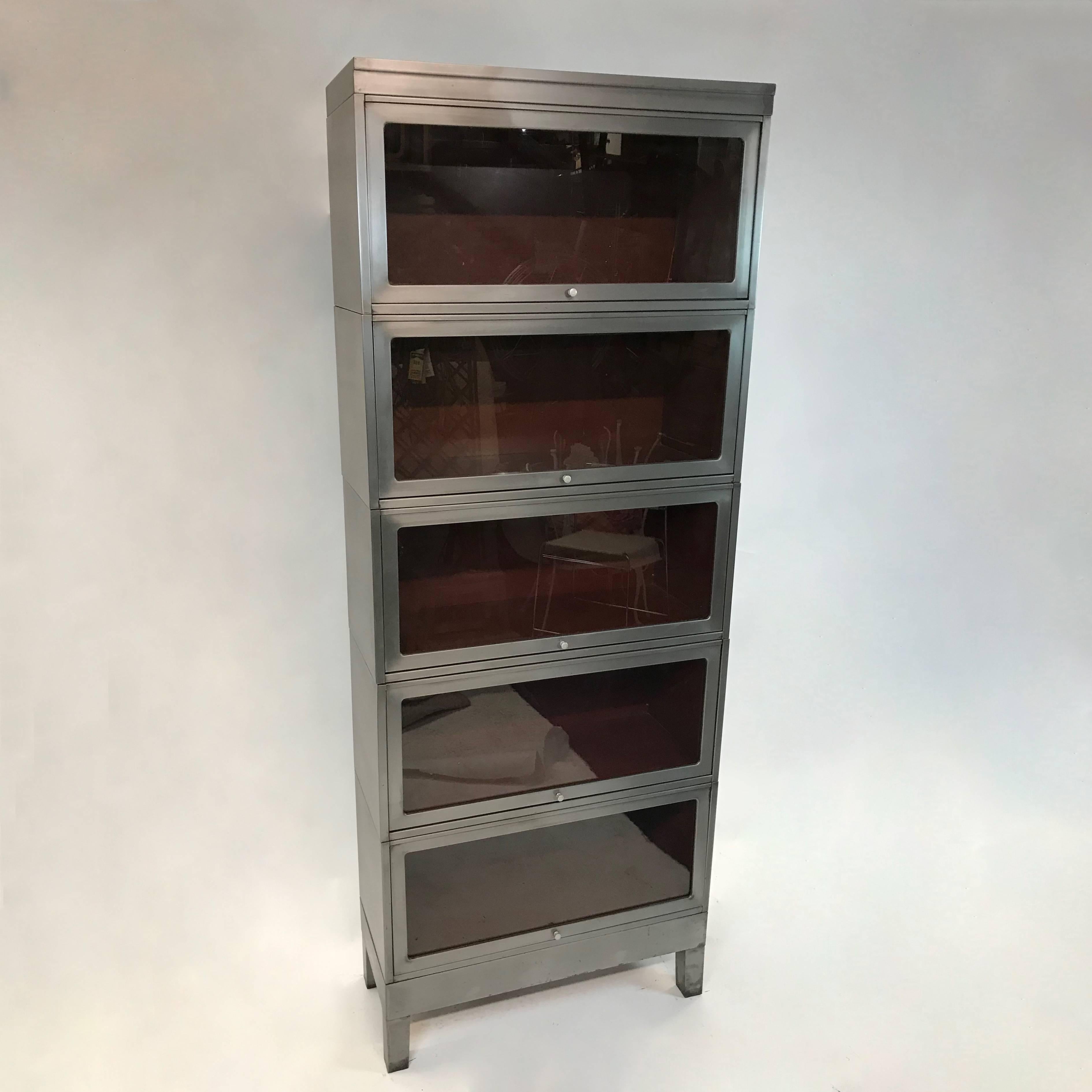 Midcentury, industrial, barrister bookcase, features six interlocking, stackable cases with glass front doors that slide to open has a newly brushed steel exterior and contrasting, original maroon paint interiors. Each case is 14.75 inches height