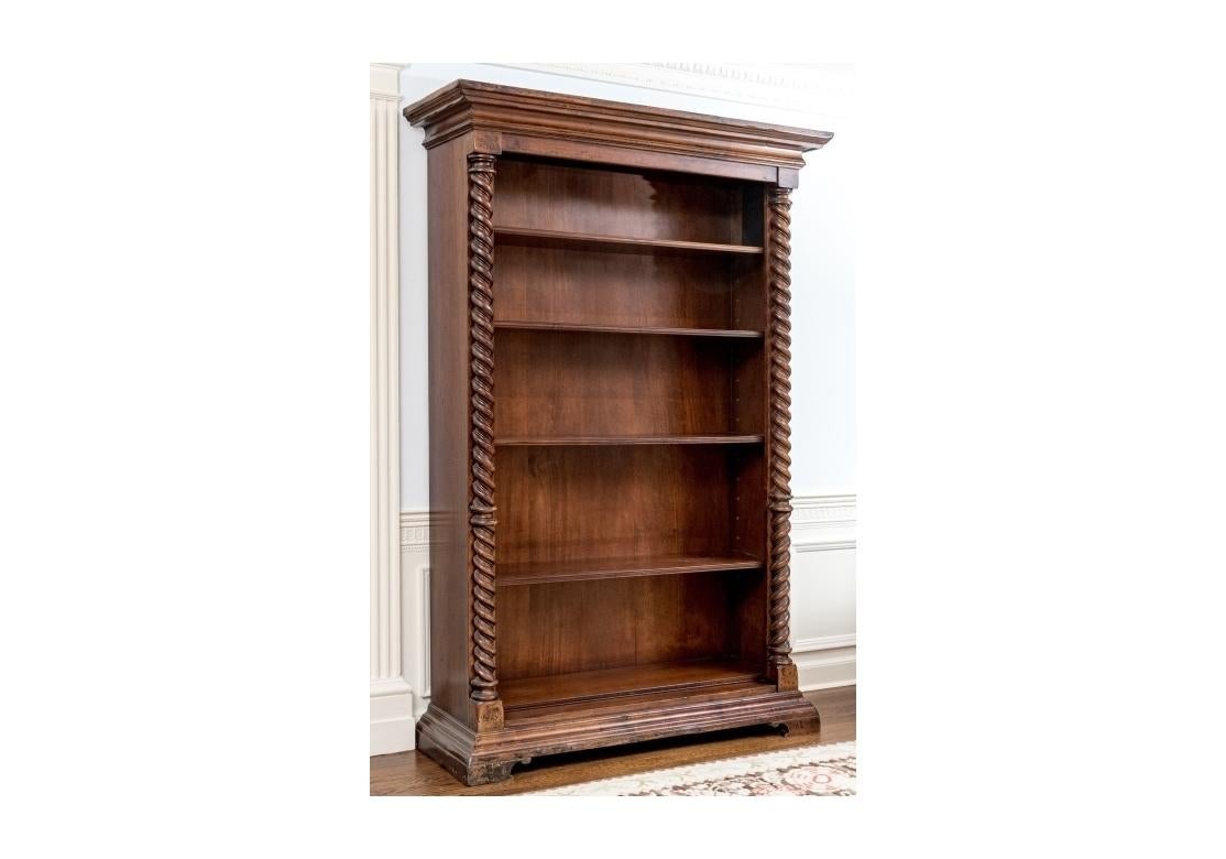 A tall open bookcase in a dark stain with bold barley twist style columns flanking five adjustable shelves. The bookcase with brass grommet form shelf pin sleeves, solid wood backing, tiered cornice and the whole resting upon bracket feet. Marked on
