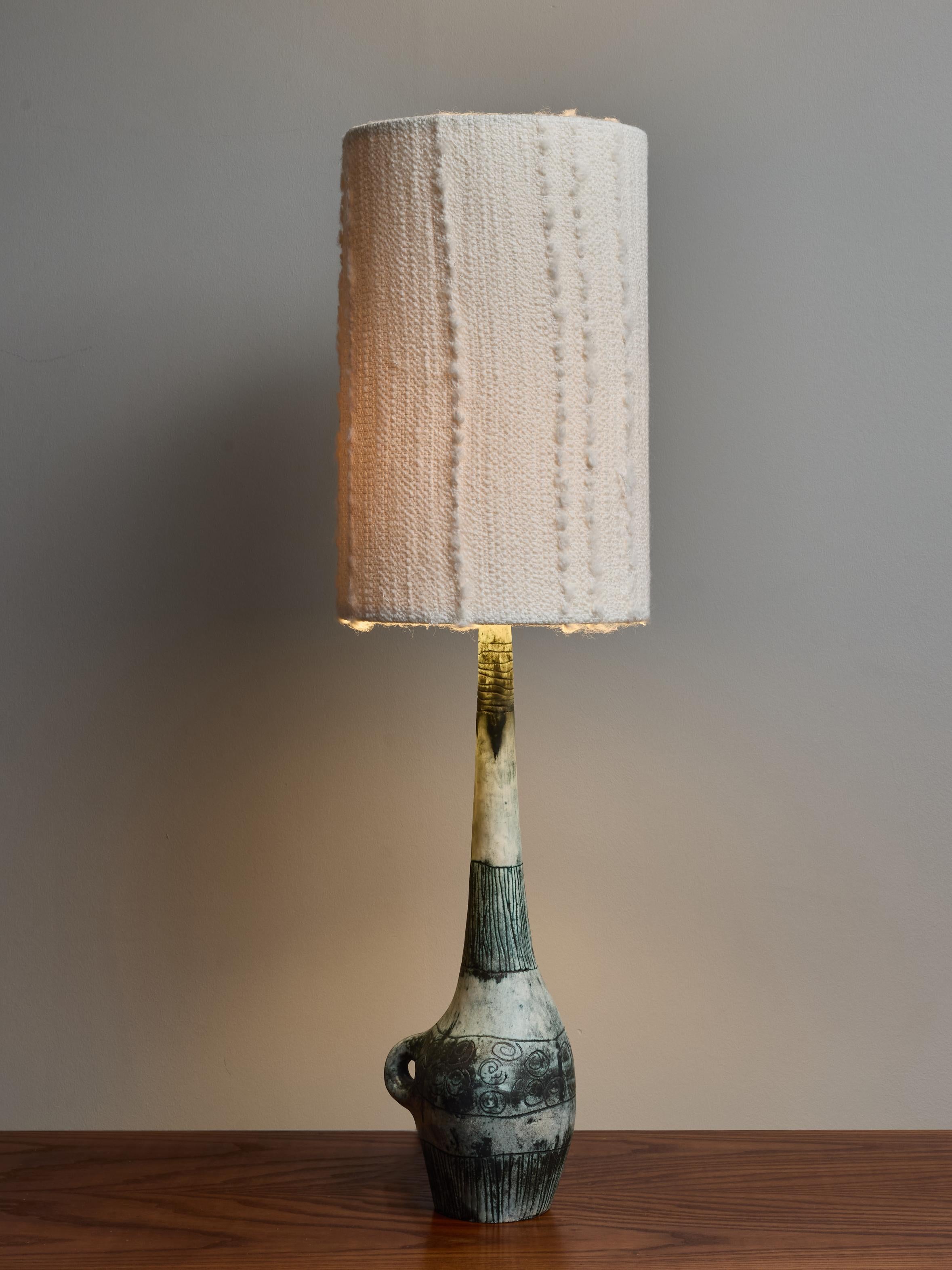 Tall ceramic table lamp by french artist Jacques Blin.

Signed at the bottom, this bottle shape lamp, with its handle and long neck has distinctive faded green glaze with floral carved decors.

Topped with a modern shade. Height with the shades: