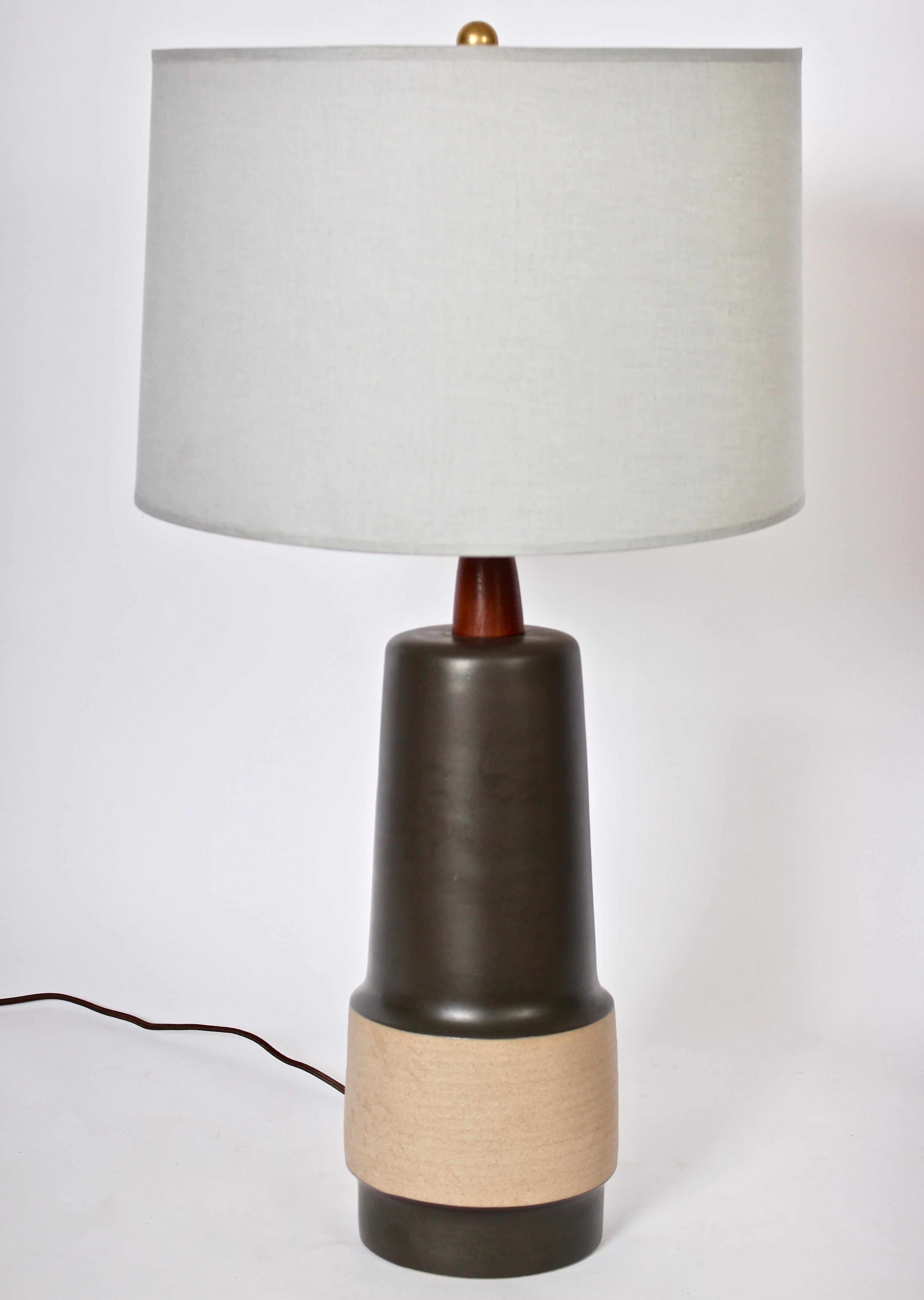 Gordon & Jane Martz Marshall Studios M144-45-D103A glazed stoneware table lamp, 1960s. In matte black with neutral Beige incised waist and turned wooden neck. 21H to top of socket. Ceramic 15H. Shade shown for display only (11H x 15D top x 16D