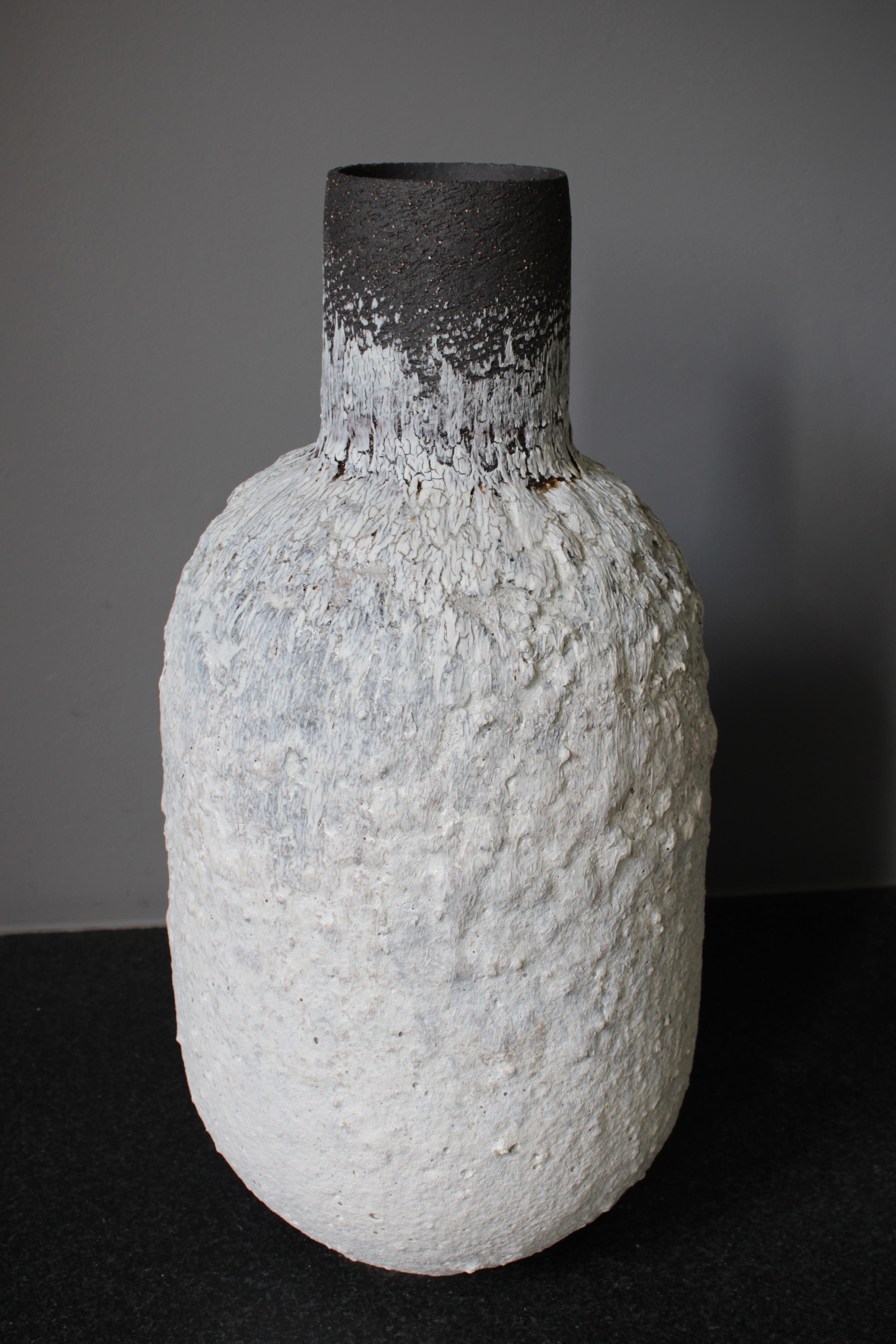 Grand récipient en forme de bouteille en grès blanc et noir et en porcelaine avec une glaçure à texture volcanique.

L'œuvre est construite à la main en utilisant une combinaison d'argiles noires et chamoisées en grès, des engobes volcaniques sont