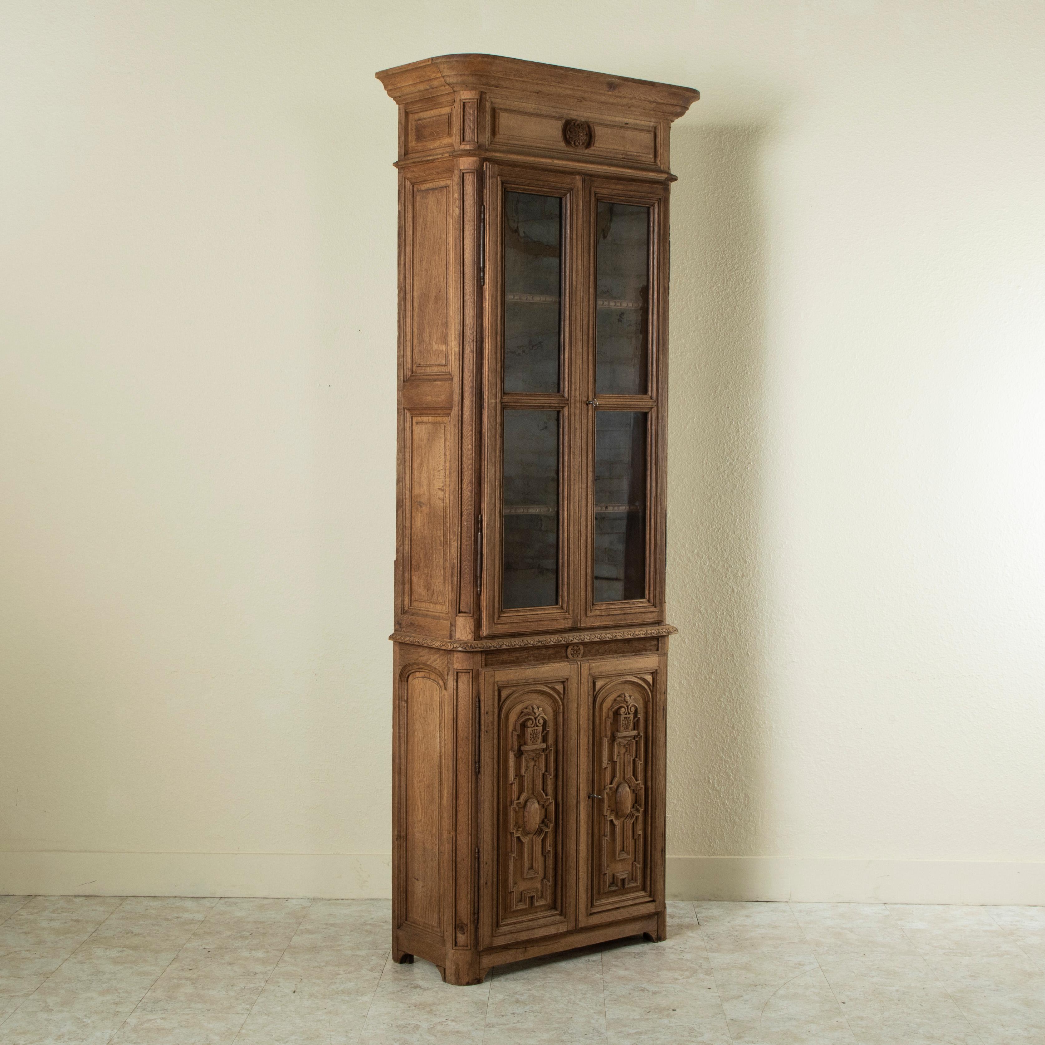 Standing just over 8 feet in height, this tall, narrow late nineteenth century French Henri II style bleached oak bookcase or vitrine features two upper doors with their original hand blown glass. The upper doors open to reveal an interior with four