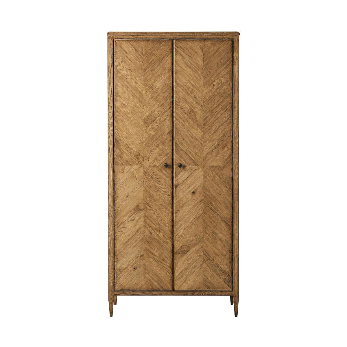 A tall light oak two door cabinet, with mirrored herringbone parquetry doors. It is adorned with elegant Verde Bronze knobs and rests upon tapered legs for added support. It is shown in our Dawn finish. 
Shown in Dawn Finish
Dimensions: 38