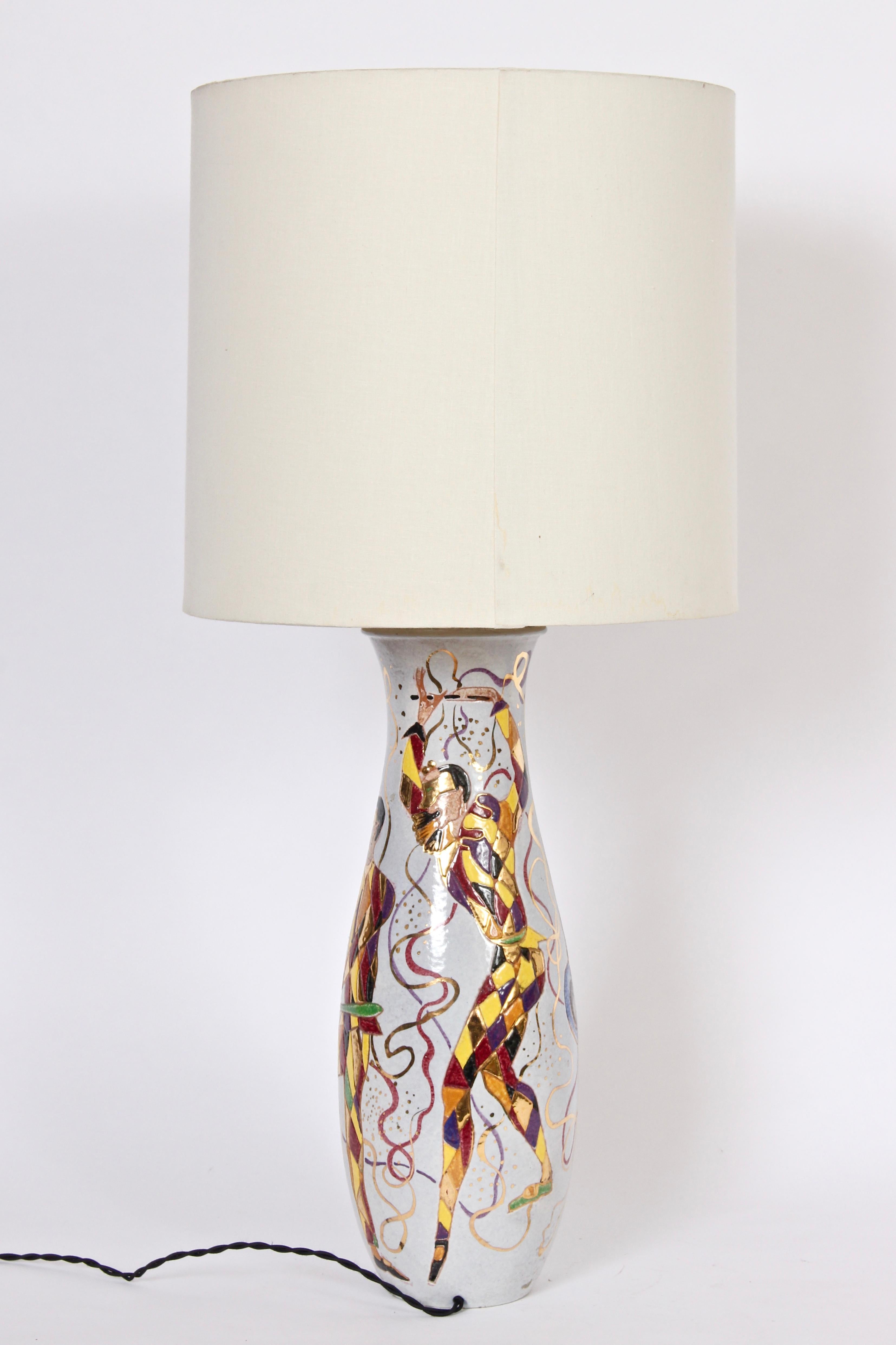 Tall Marcello Fantoni bright Masquerade glazed ceramic Table Lamp, circa 1950. Featuring a reflective white background and hand painted textured ribboned, masked, dancing, harlequins in green, yellow, gold copper, red & maroon. 22 H to top of