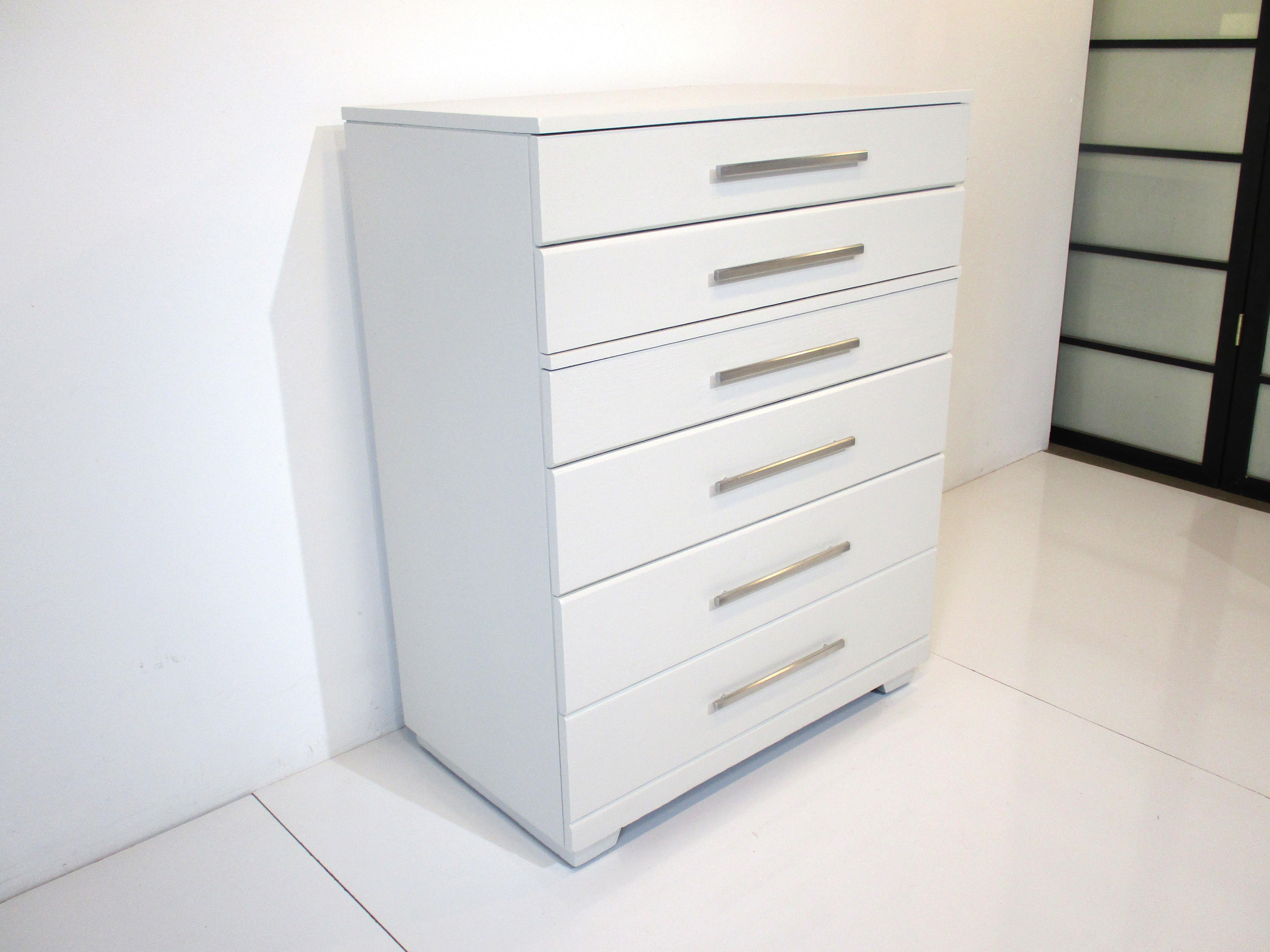 A chalk white very well constructed six drawer tall dresser chest with long thin aluminum pulls. By the iconic designer Raymond Loewy who touched most of American life with designs for appliances, trains, automobiles like the Studebaker Avanti,