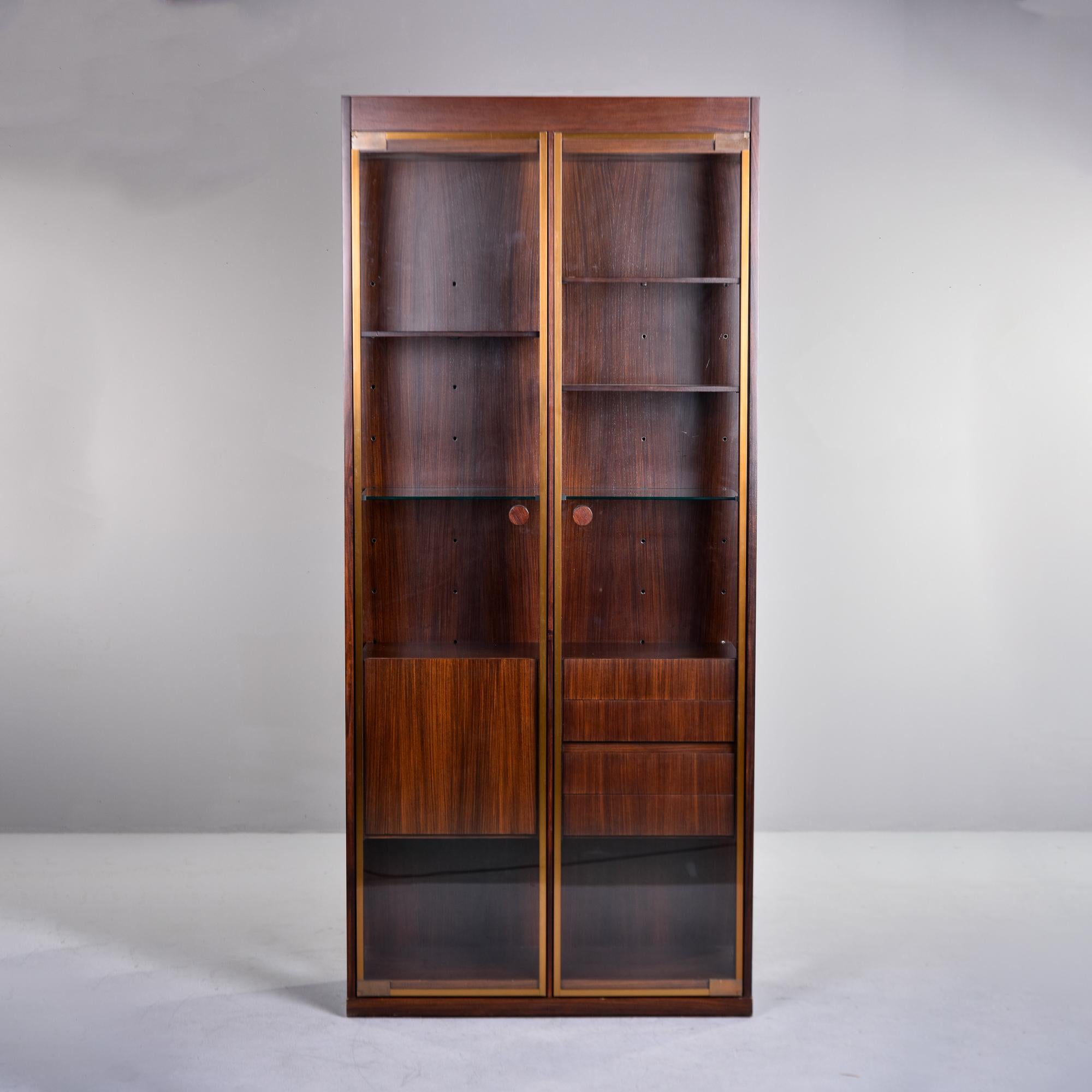 Found in France, this tall walnut and glass cabinet has a combination of drawers, adjustable shelves and compartment storage. Two glass doors with brass edge trim open to a stack of four drawers, adjustable wood and glass shelves, a fold down