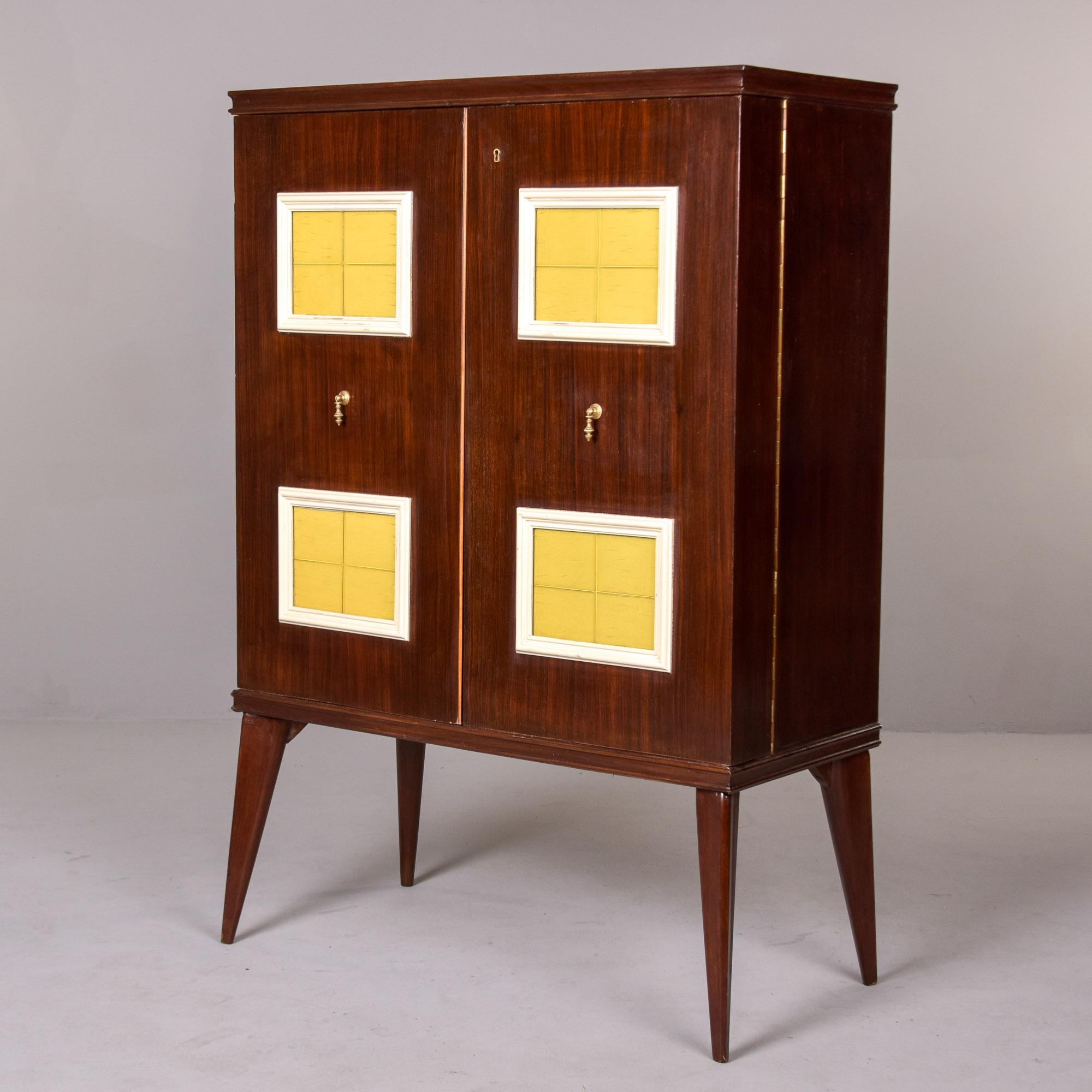 Dieser Barschrank aus Nussbaumholz wurde in Italien gefunden und stammt aus den 1950er Jahren. Dieser Schrank hat zwei verschließbare Flügeltüren mit gelben Glaseinsätzen und Messingbeschlägen. Verjüngte Beine, Innenausstattung mit verspiegeltem