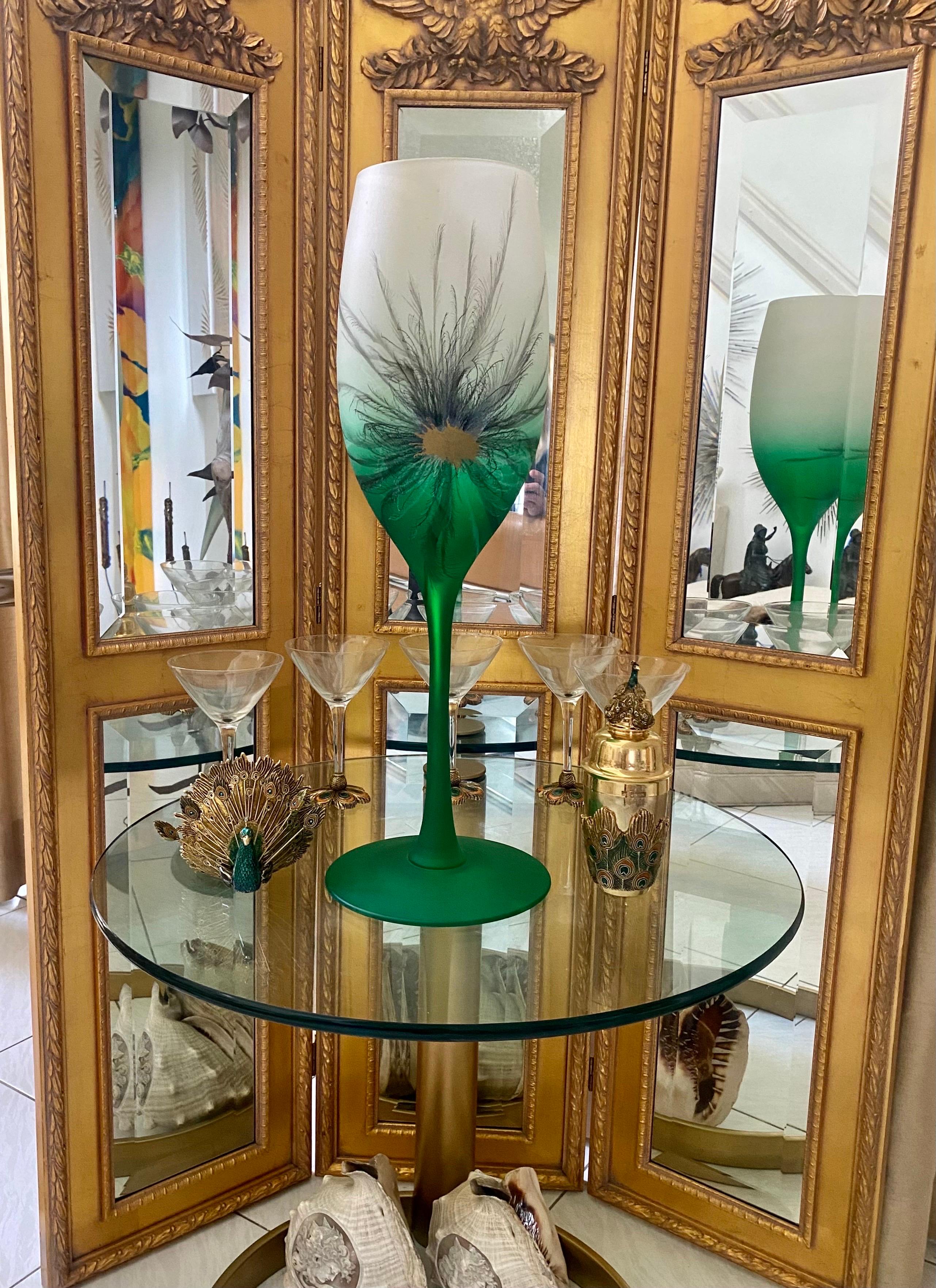 Tall two tone glass goblet shaped vase in an emerald green color that fades to white. The vase has been hand painted in a delicate feather pattern with a gold center, reminiscent of a peacock feather.