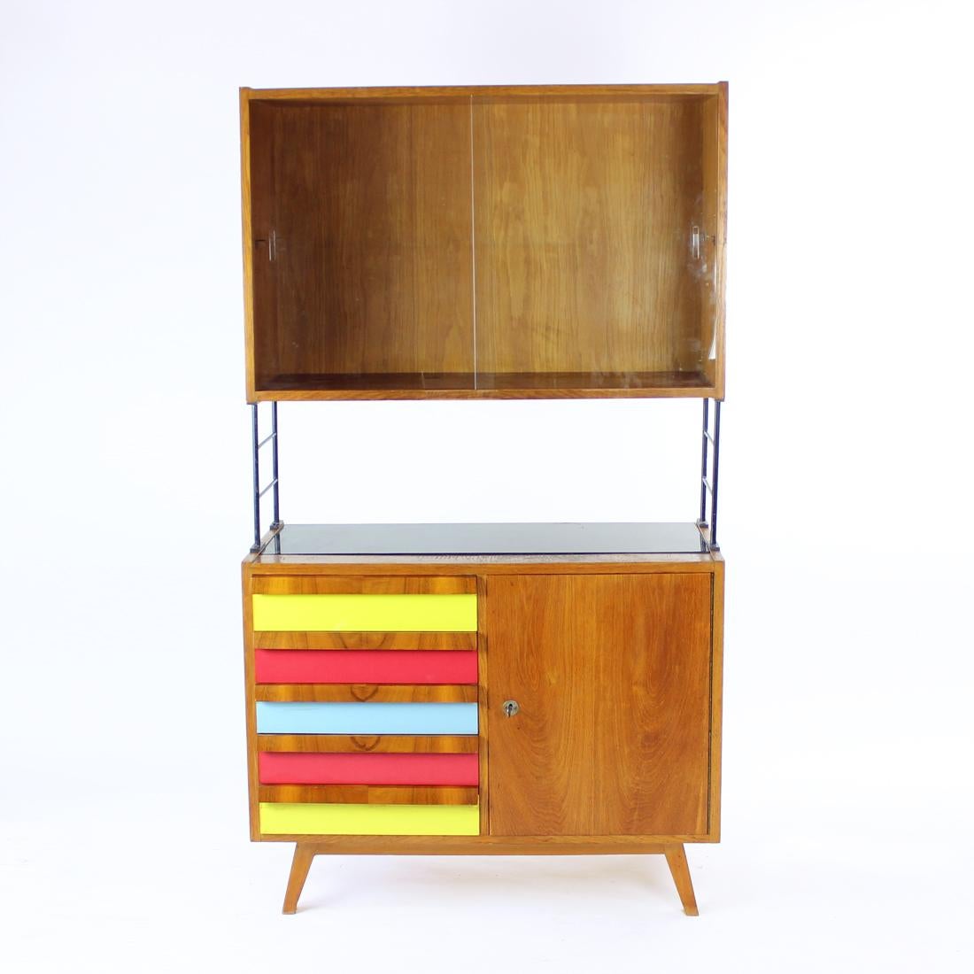 Beautiful tall mid-century cabinet with typical featured and details of the era. Produced in Czechoslovakia in 1960s. This cabinet is made of strong materials. The bottom sideboard part is made of oak wood with five colorful drawers and walnut