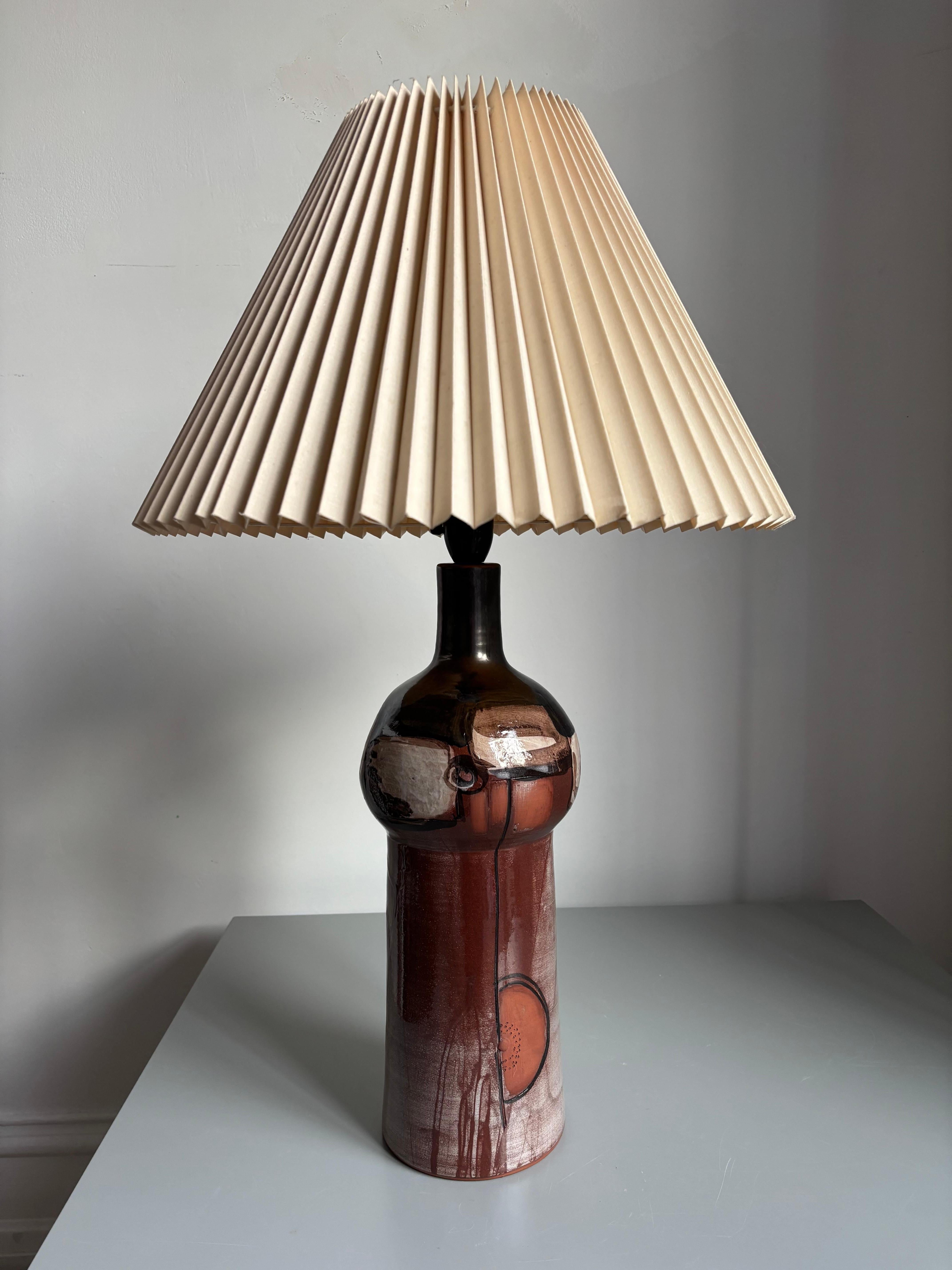 Large ceramic art table lamp with earthy colors over abstract hand-carved decorations on the tall, soft curved body. Black, brick red, cream, dark and light brown colored shiny glaze.
Signed under base.
Beautiful vintage condition. 
Denmark,