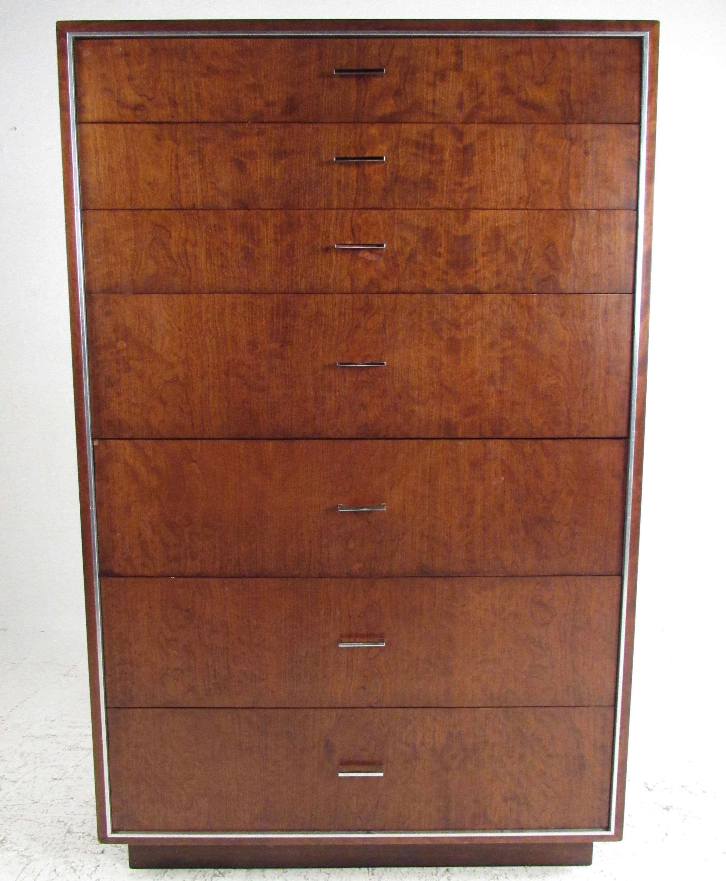 This tall midcentury dresser by John Stuart Inc. features warm walnut tones accented by aluminium trim and chrome drawer pulls. This substantial mid-century highboy makes an impressive dresser in any bedroom setting, offering seven graduated drawers