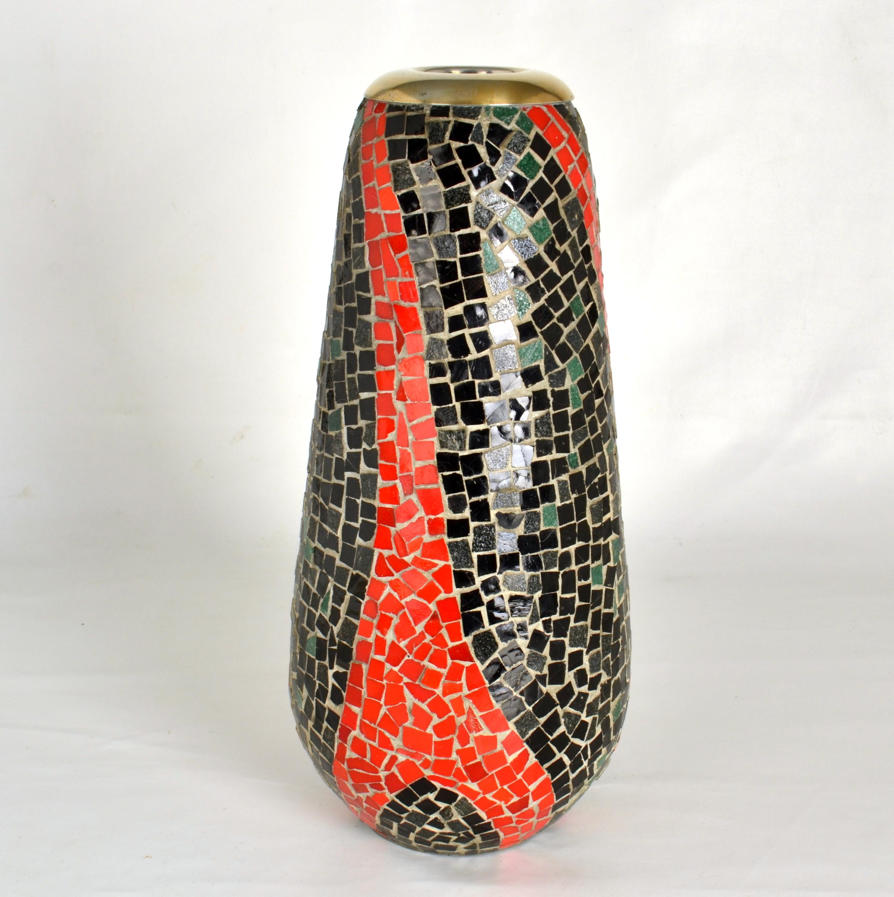 Hohe Vase mit einem organischen Mosaikmuster aus nachtschwarzen und tomatenroten Glasstücken. Das Mosaik wird angewendet auf  eine Glasvase, die als funktionelle Blumenvase dient und mit einem Messingrand versehen ist. Die Öffnung hat einen