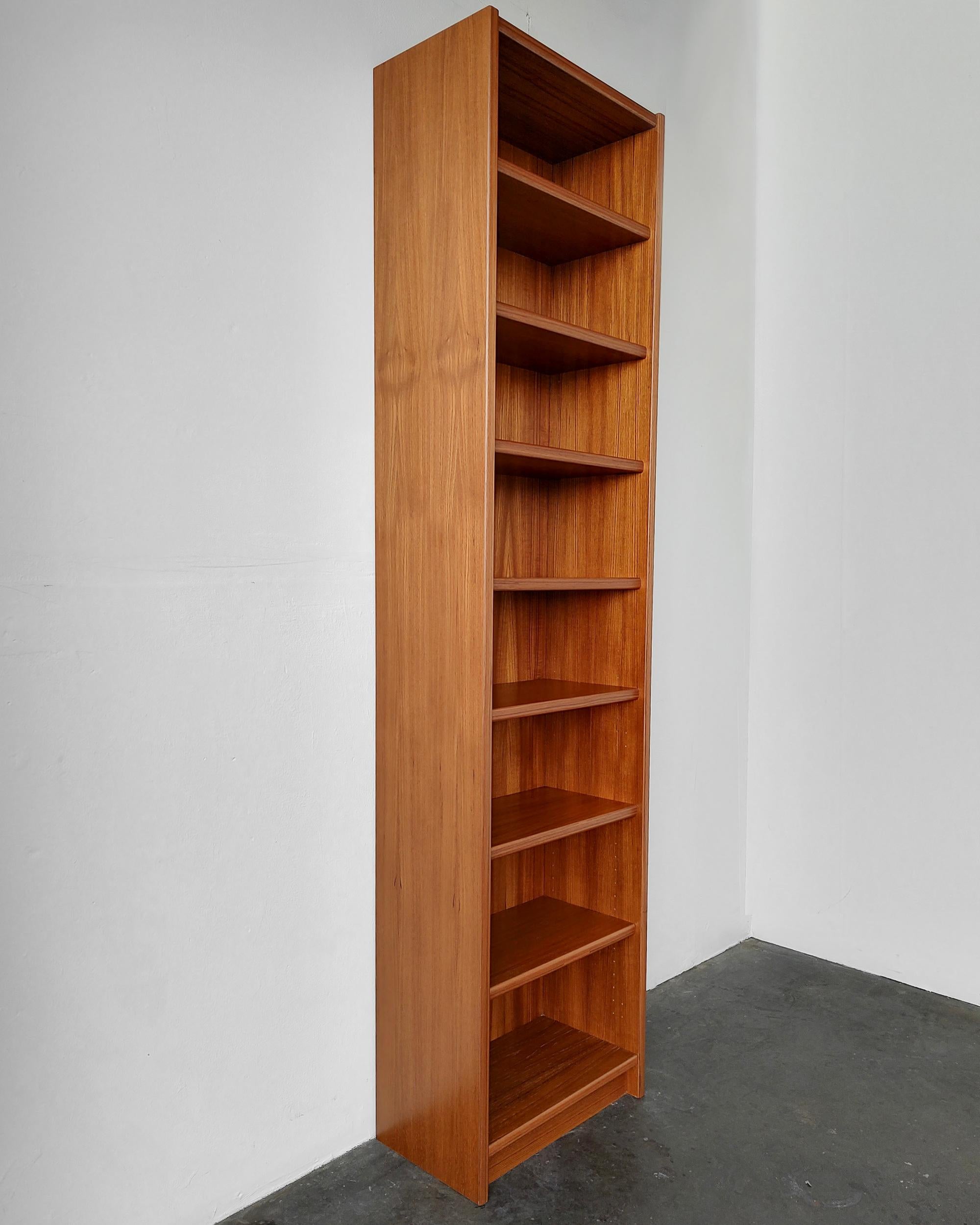 Tall narrow Danish mid-century modern teak wood bookshelf. Two fixed shelves, all others are adjustable. A couple of discolored lines on the right upper side (see photo). No chips in veneer, great vintage condition. May have sun lines if the the