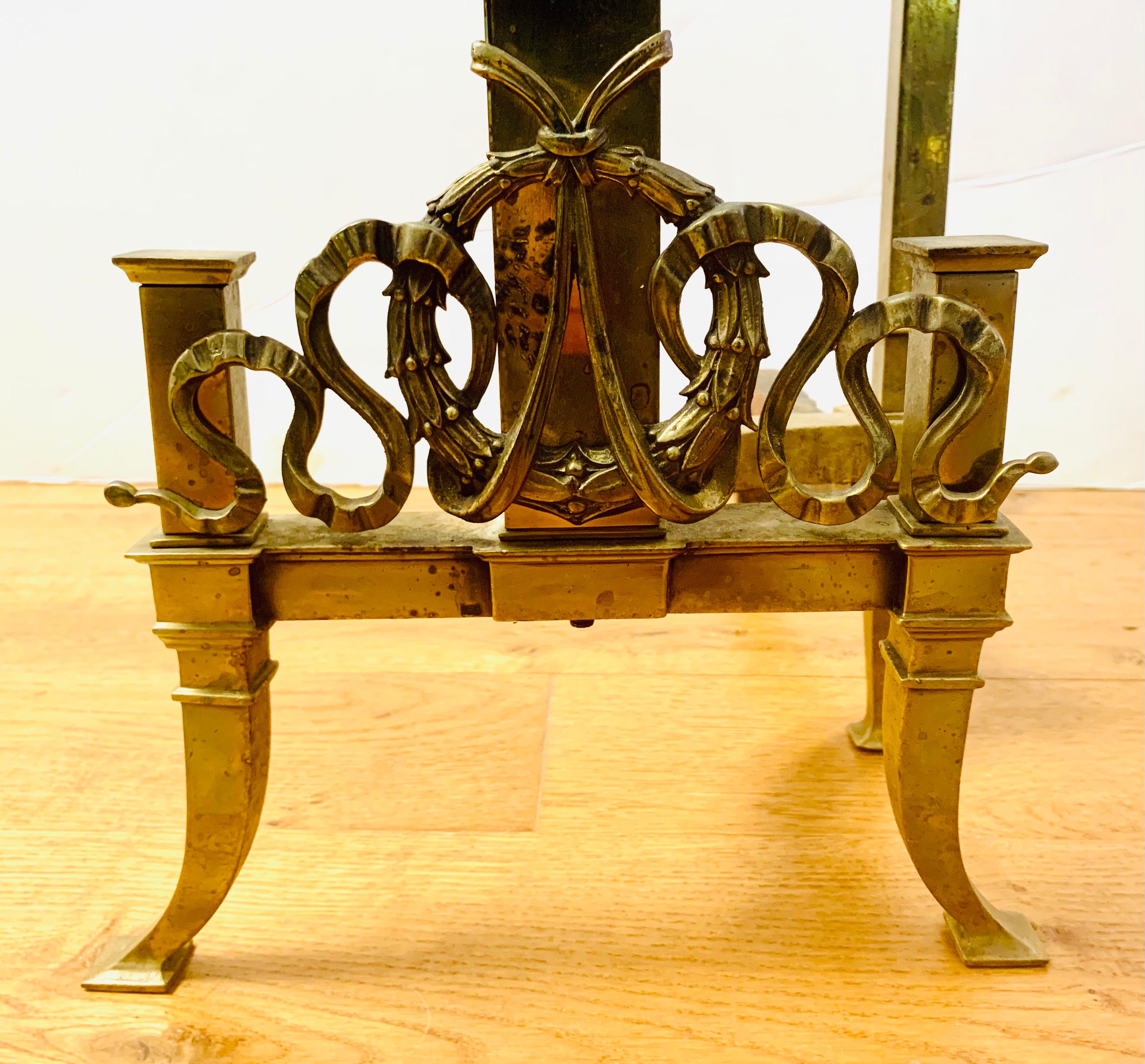 Beautiful pair of brass square column form andirons with footed base decorated with wreath and ribbons.