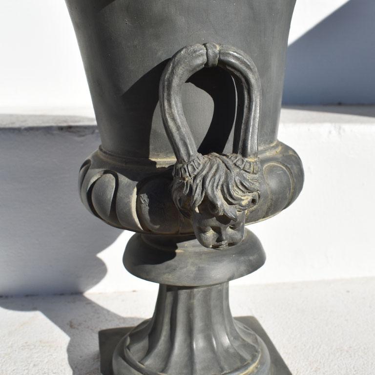 A tall neoclassial style Jardinière with cherub handles. This pretty planter is tall, and deep gray in color. It stands upon a square base and features two faux bois handles with small cherubs at the bottoms. This would be an excellent addition to a