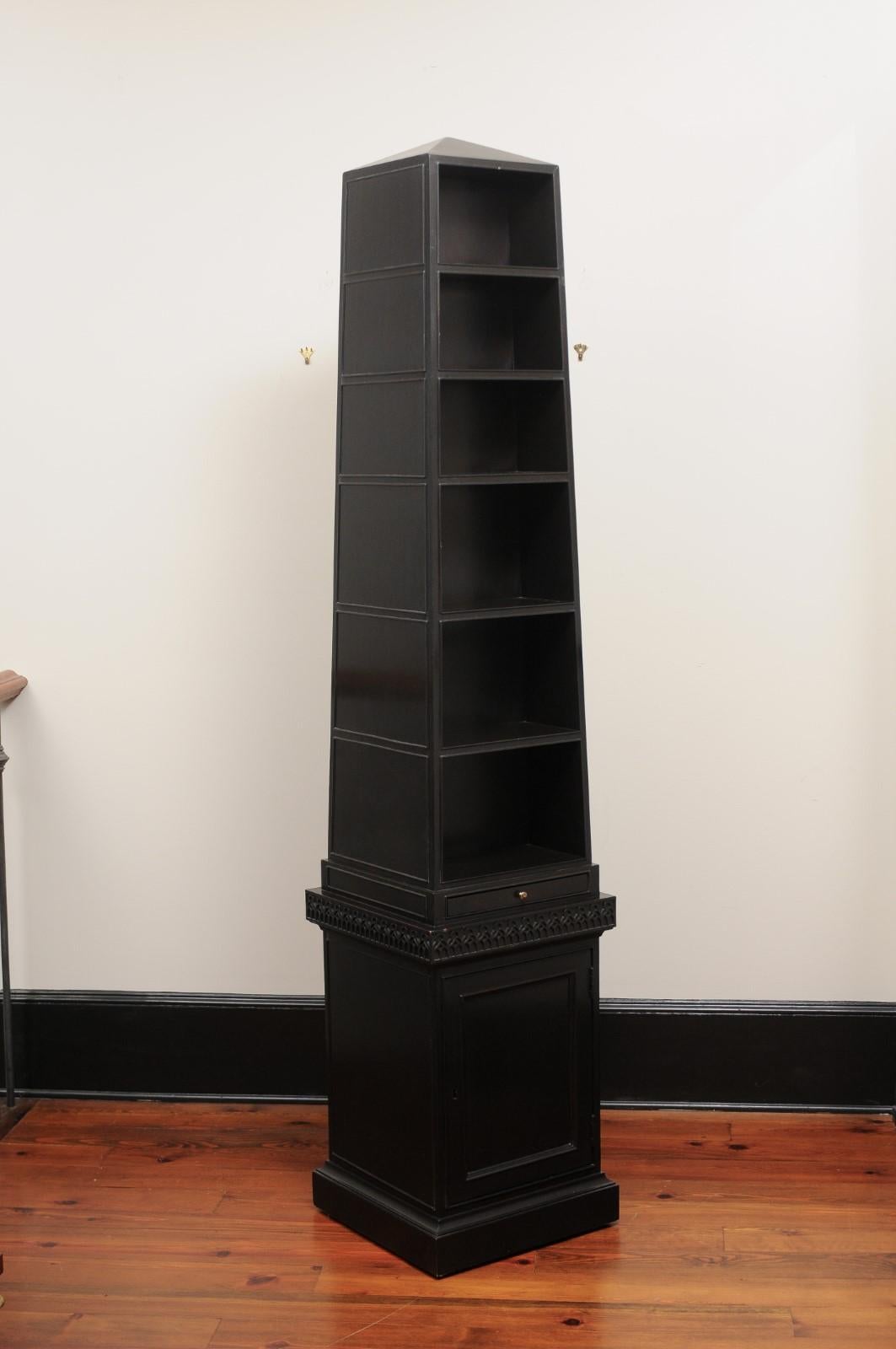 A fine mahogany four- sided bookcase, formed as an obelisk or pyramid on a roller base to reveal various compartments and shelves, with cupboards below on a square plinth, the entire bookcase decorated and designed with finely carved fretwork.