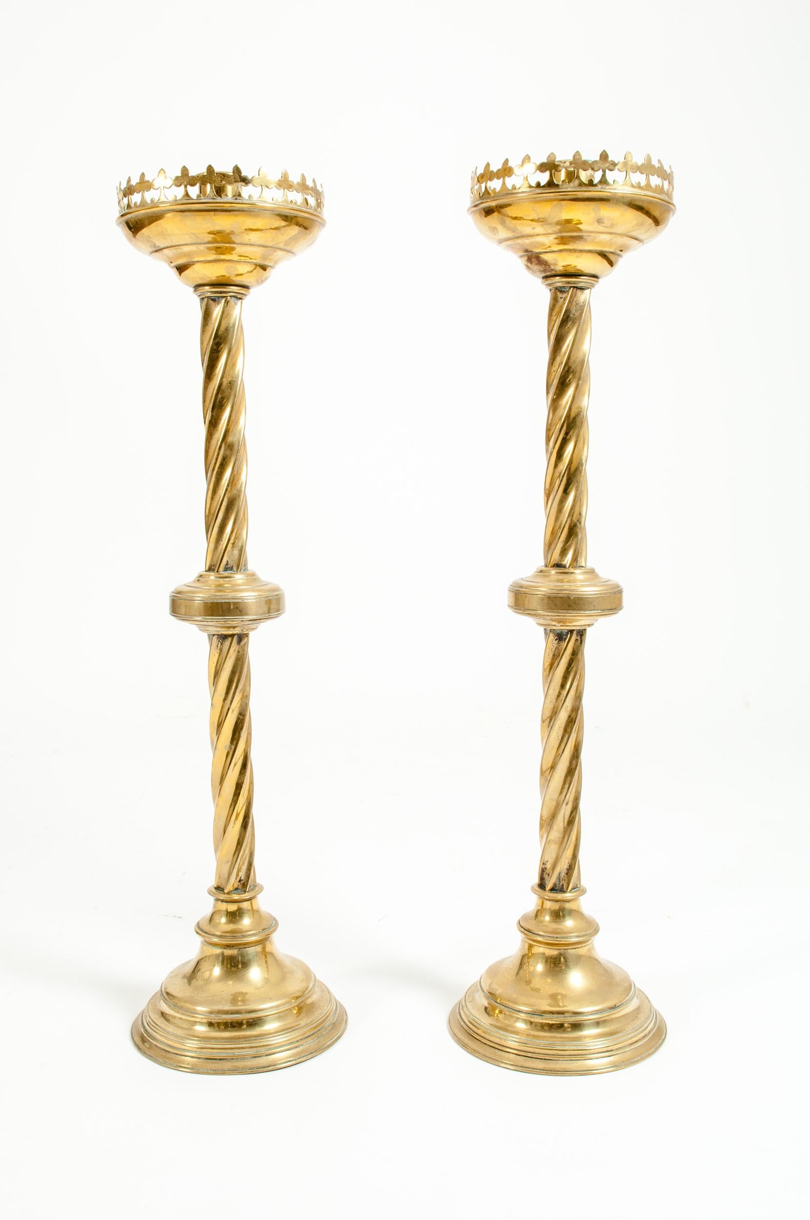 Tall and ornately decorative pair of late 19th century Gothic style brass candlesticks. The candlesticks consist of a candleholder to the top with a rimmed edge with a drip pan with a trefoil pierced gallery of typical Gothic design. And leads down