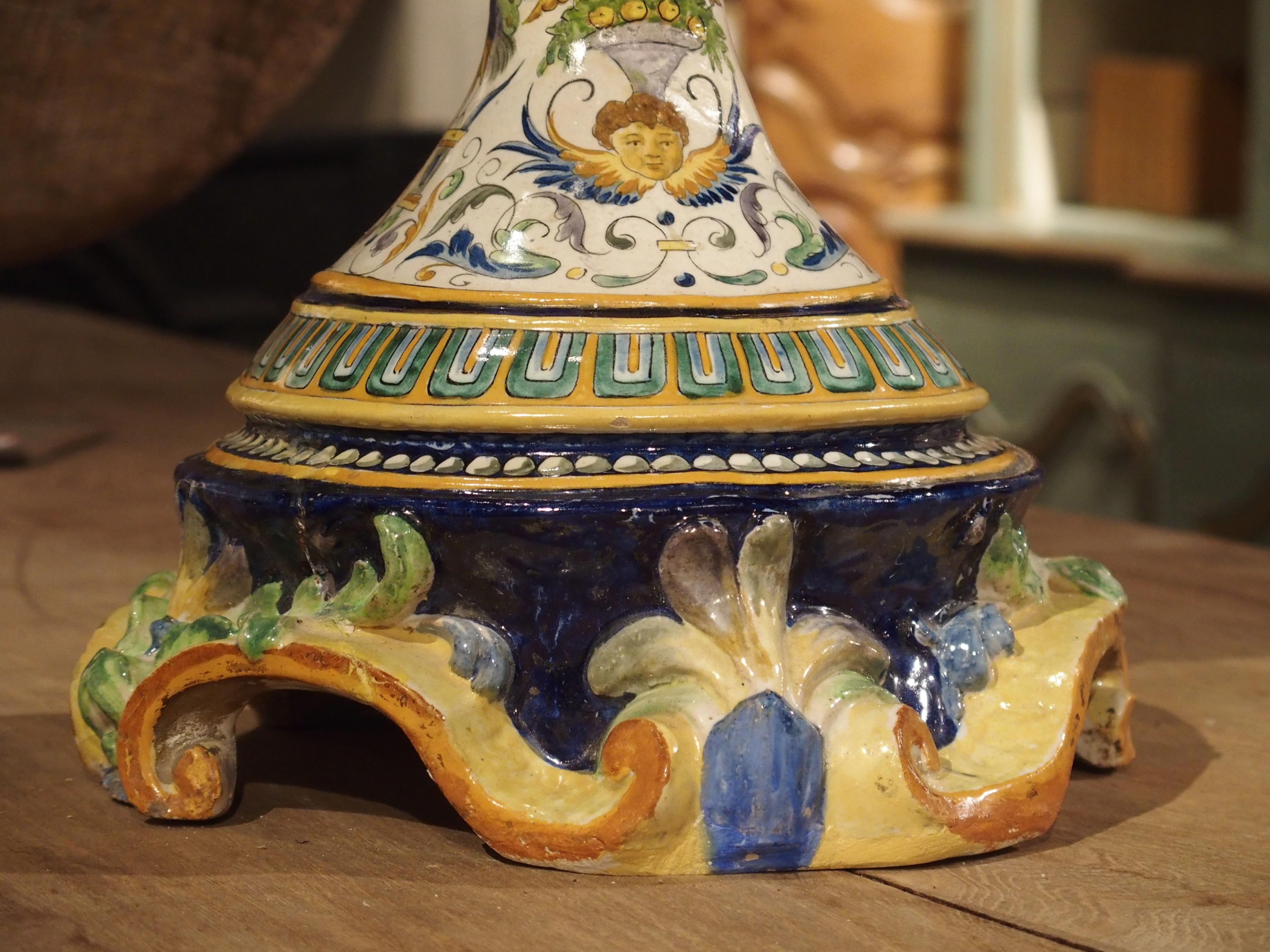 From Italy, this imposing antique hand-painted Majolica vase with handles is nearly 39 inches high. It is mainly a figural vase in style, having beautiful hand-painted scenes within cartouches on either side. The motifs throughout the rest of this