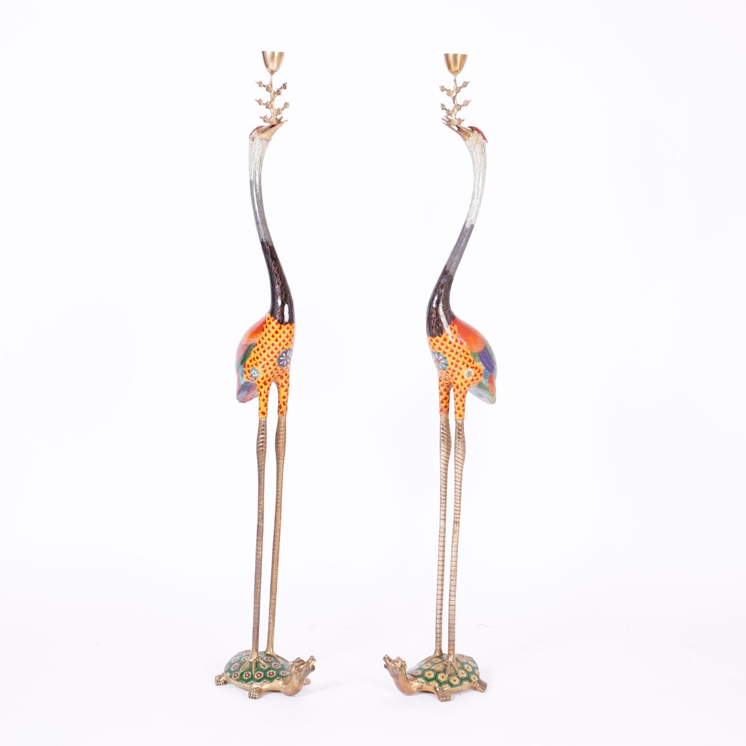 Pair of Chinese cloisonné or enamel on brass cranes or storks holding candle cups in their beaks. The birds are decorated with colorful stylized feathers and stand on enameled turtles with dragon heads.