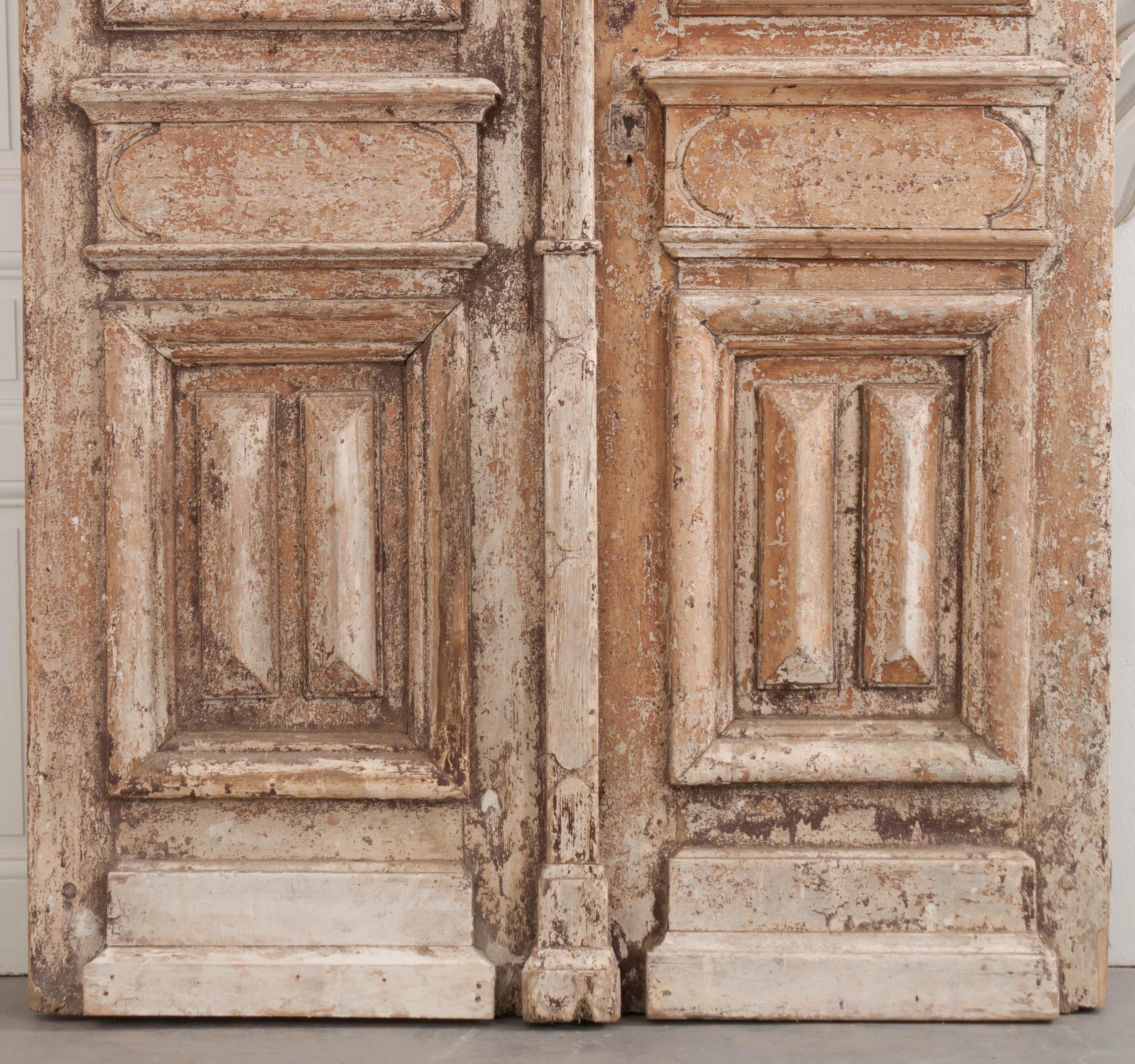 This tall and imposing pair of Napoleon III-style painted-pine and wrought iron entry doors are from France, circa 1900s, and retain the original richly patinated cream-colored paint. Each deeply carved and paneled door is outfitted with restored
