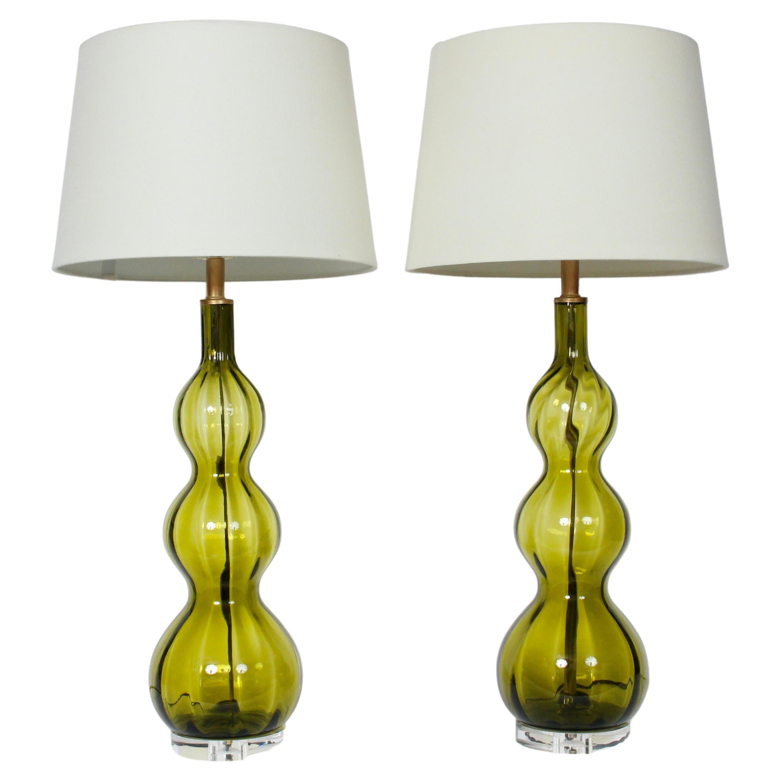 Substantial pair of organic modern ribbed olive green glass table lamps. 
Featuring a tall, triple gourd hand blown translucent Army Green coloration, Brass necks, atop (6D x 1H) clear Lucite bases. 26.5H to top of Socket. 21.5H to top of Glass.