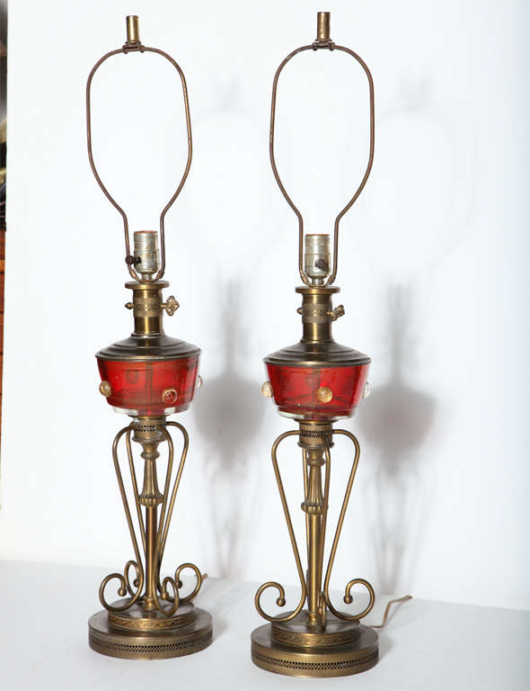 Paire de lampes de table en verre Murano rouge et laiton de style Hollywood Regency, vers 1950. La lampe est de style lampe à huile, le centre est en verre de Murano rouge translucide avec des inclusions rondes dorées, la tige supérieure est en