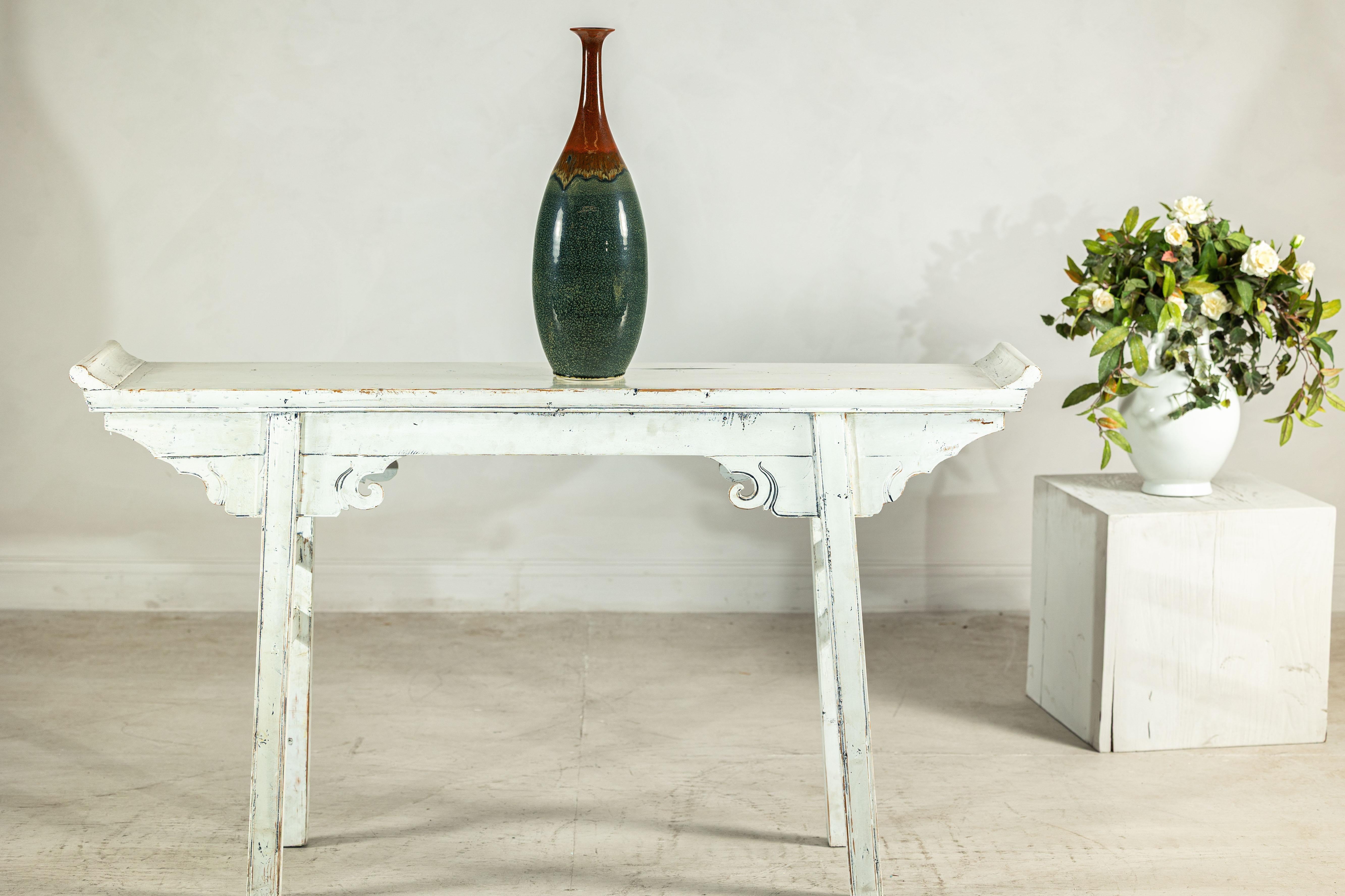 With its striking blend of textures and color transitions, this tall stoneware vase brings a refined yet earthy presence to any setting. The form is distinctly sculptural: a smooth, elongated ovoid body rises seamlessly into a narrow neck that opens