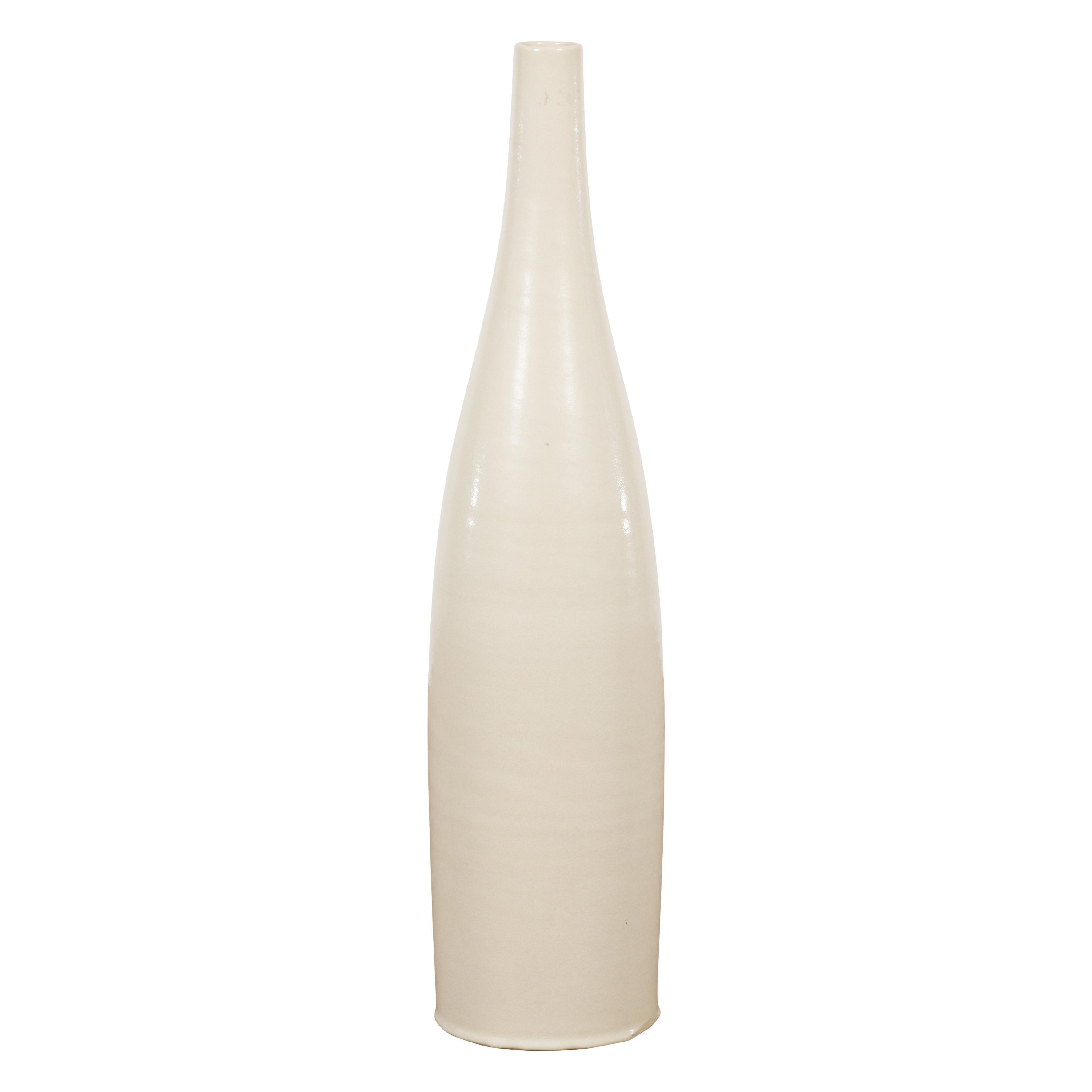 A tall contemporary Prem Collection artisan made vase with cream glaze and slander silhouette. This tall vase is a product of the Prem Collection. Its slender silhouette, capturing grace and sophistication, is accentuated by a creamy, neutral glaze