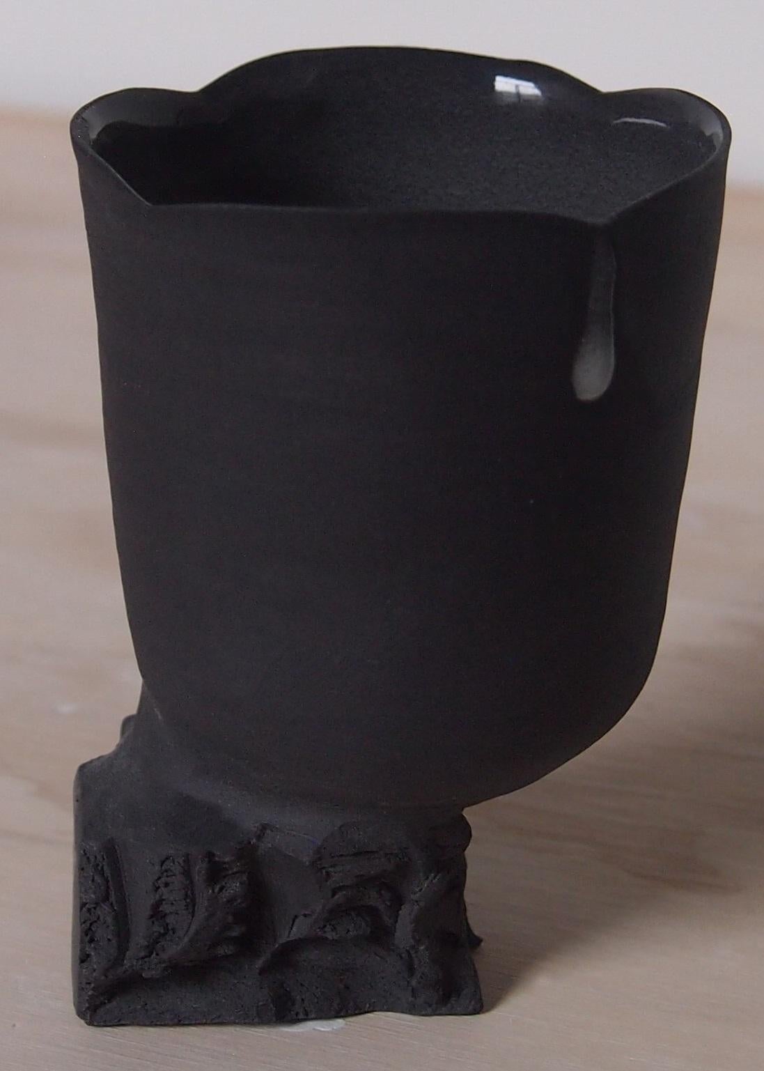 Tall Quarry Cup by Liyang Zhang
One Of A Kind.
Dimensions: D 6,5 x W 6,5 x H 10 cm.
Materials: Black porcelain. 

Made with single peice of black porcelain. The top is made on the wheel and bottom is made by tearing and chiselling.  The form reveals